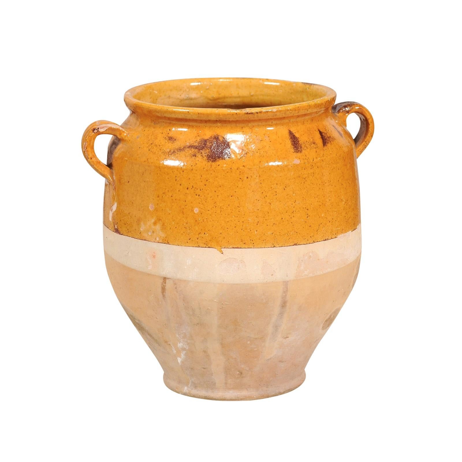 A French Provincial pot à confit pottery from the 20th century with yellow glaze, two lateral handles and rustic patina. This French Provincial pot à confit pottery piece from the 20th century is a charming representation of rustic French country
