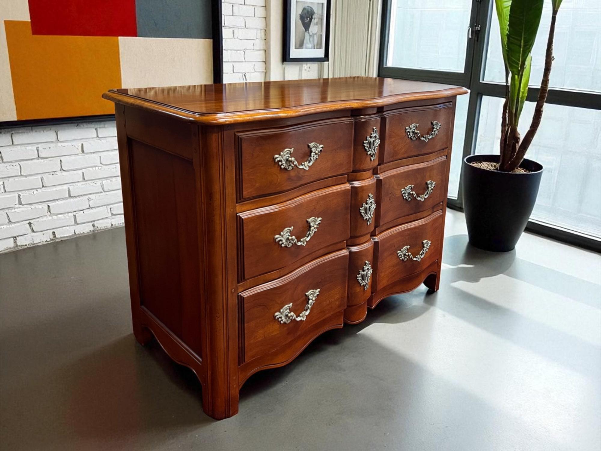 Questo comodino in stile provinciale francese è caratterizzato da un frontale a serpentina e da una finitura in legno dai toni caldi e ricchi. È accentuato da un grembiule smerlato, elemento caratteristico dell'estetica provinciale francese.
La