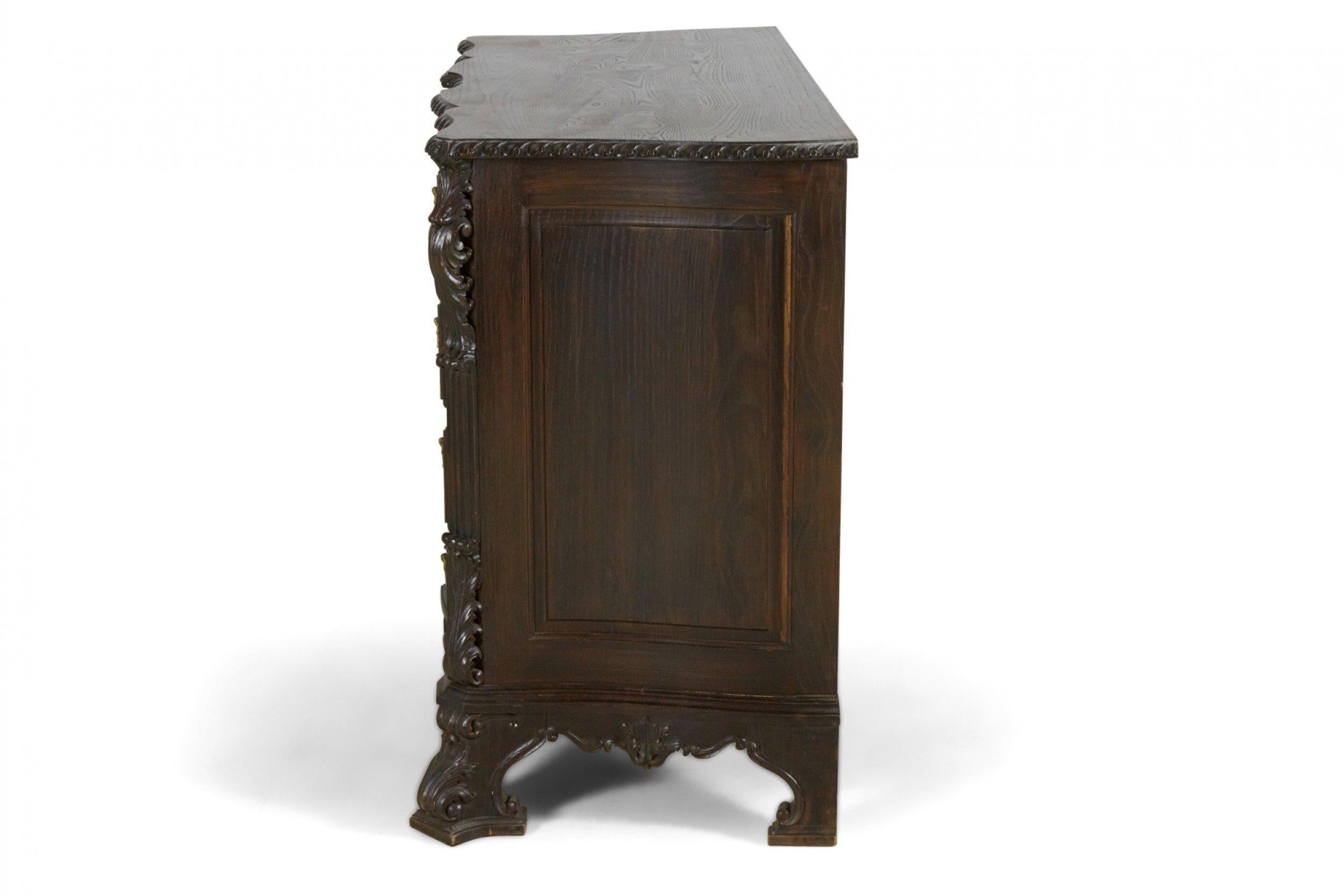 French Provincial style (20th Century) 5-drawer dresser, dark stained pine with ornate brass handles and carved features, foliate scroll sides and serpentine shaped front.
