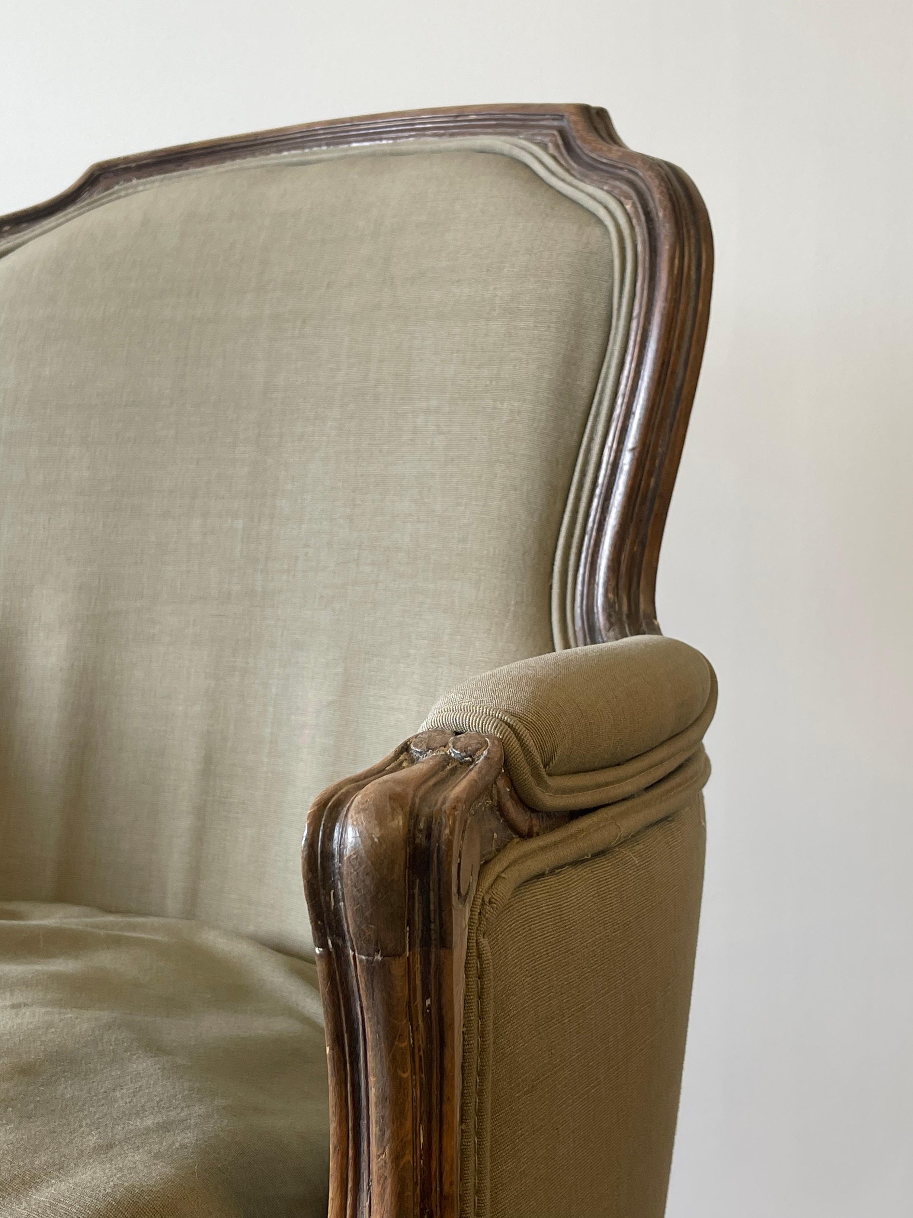 French provincial style upholstered arm chairs or bergeres, with a shaped molded crestrail above an upholstered back en cabriolet, the back, sides, and seat now upholstered in an olive green linnen, on shaped seat above cabriole legs.