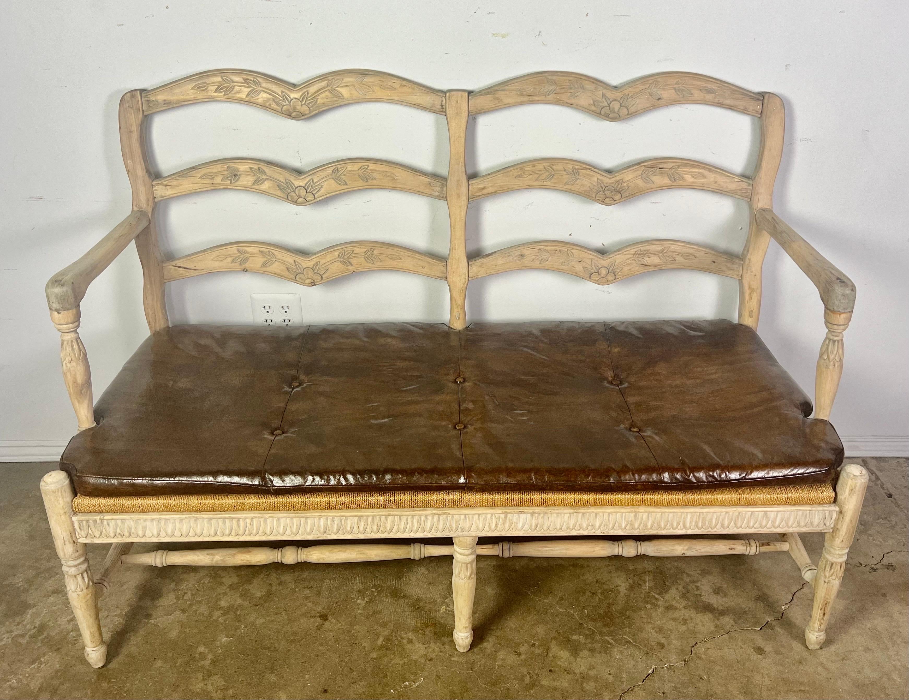 French Provincial style ladder back settee w/ leather cushion & rush seat. The bench stand on six straight legs connected by bottom stretchers. Carved flowers are added onto the frame of the sofa. There is a loose leather seat cushion for extra