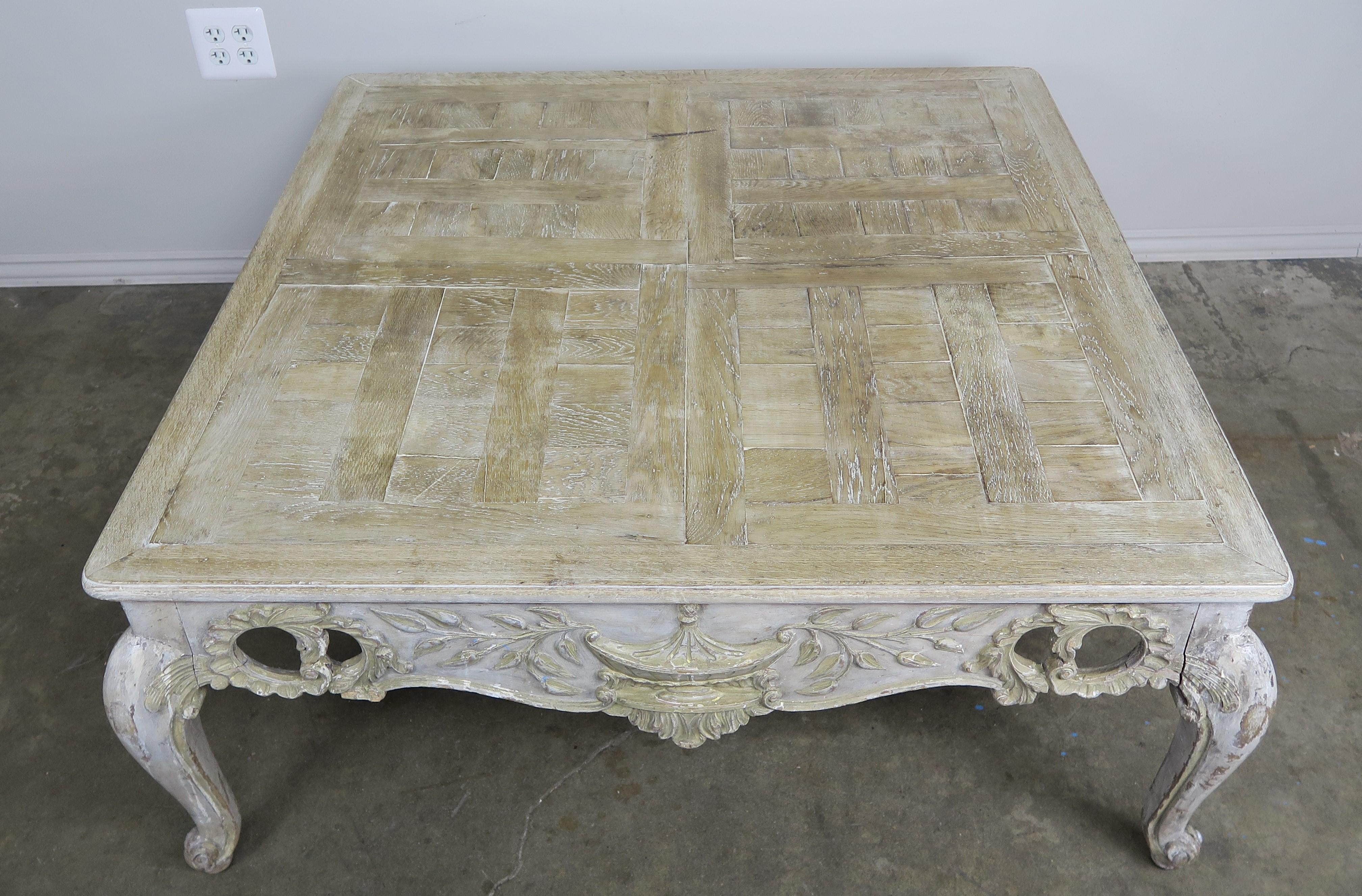 French Provincial style carved wood painted coffee table. The table has an urn carved on each side flanked by laurel leaves and beautiful acanthus leaf cut outs. The top is parquetry and sits on four cabriole shaped legs that end in rams head feet.