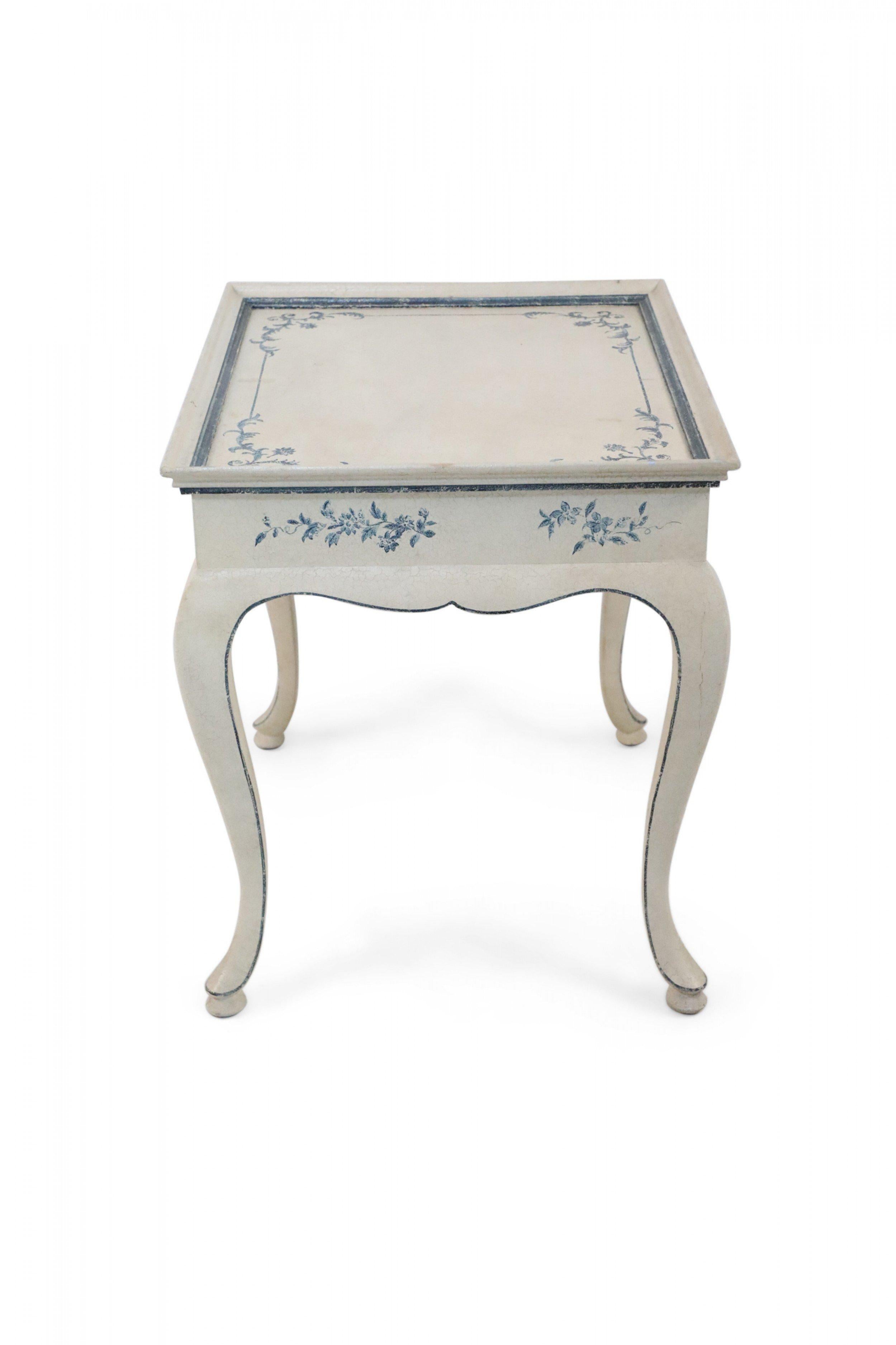 French Provincial-style (modern) cream-colored center table with a faux-distressed finish and scalloped apron and cabriole legs that are traced with a thin blue line, matching blue floral designs detailed along the top and all sides.
  