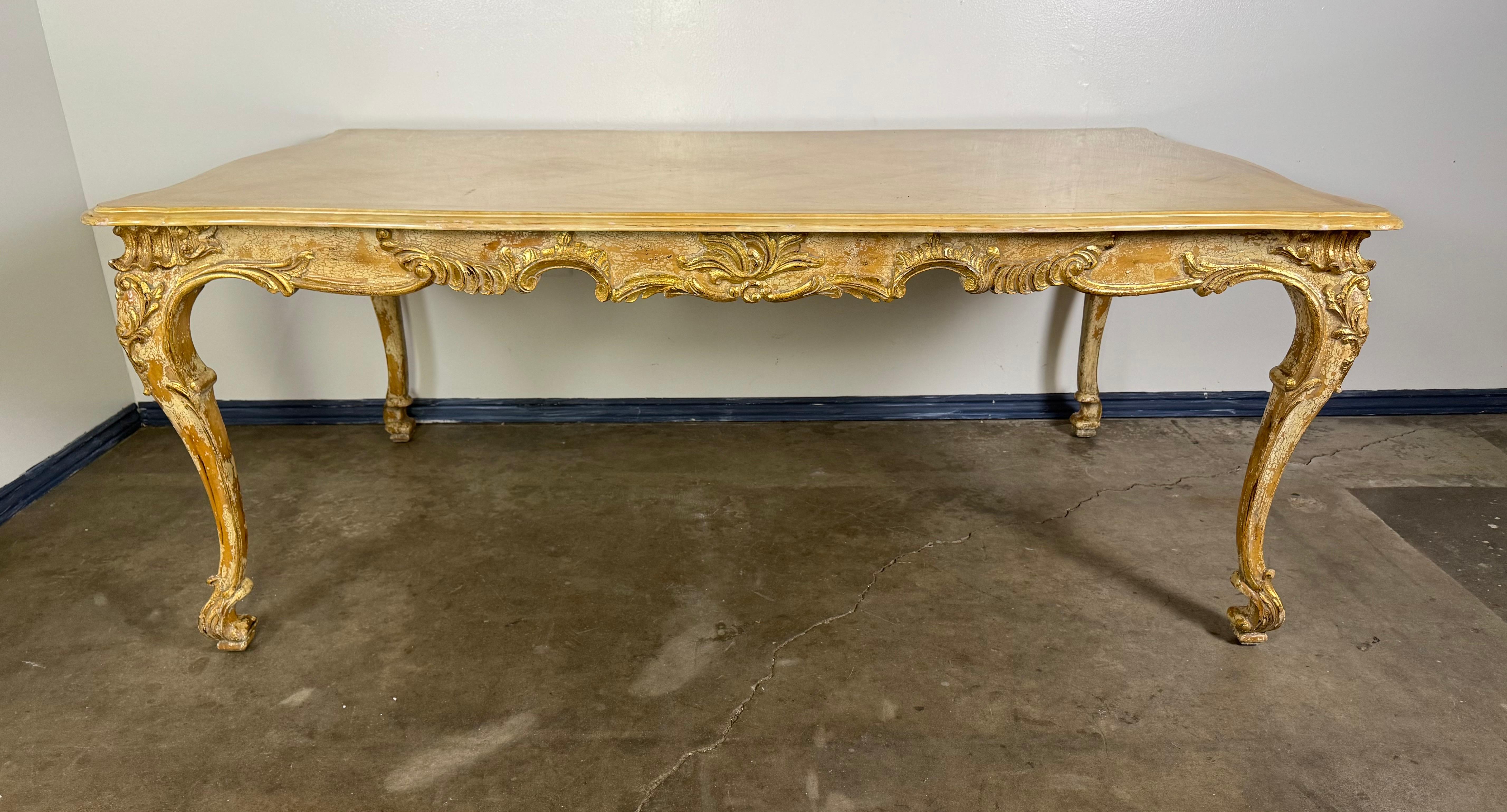 Cette table de salle à manger présente un élégant design antique avec des sculptures complexes et des détails ornés, notamment sur le tablier et les pieds cabriole. La table est fabriquée en bois avec une finition peinte en détresse légère, dans un