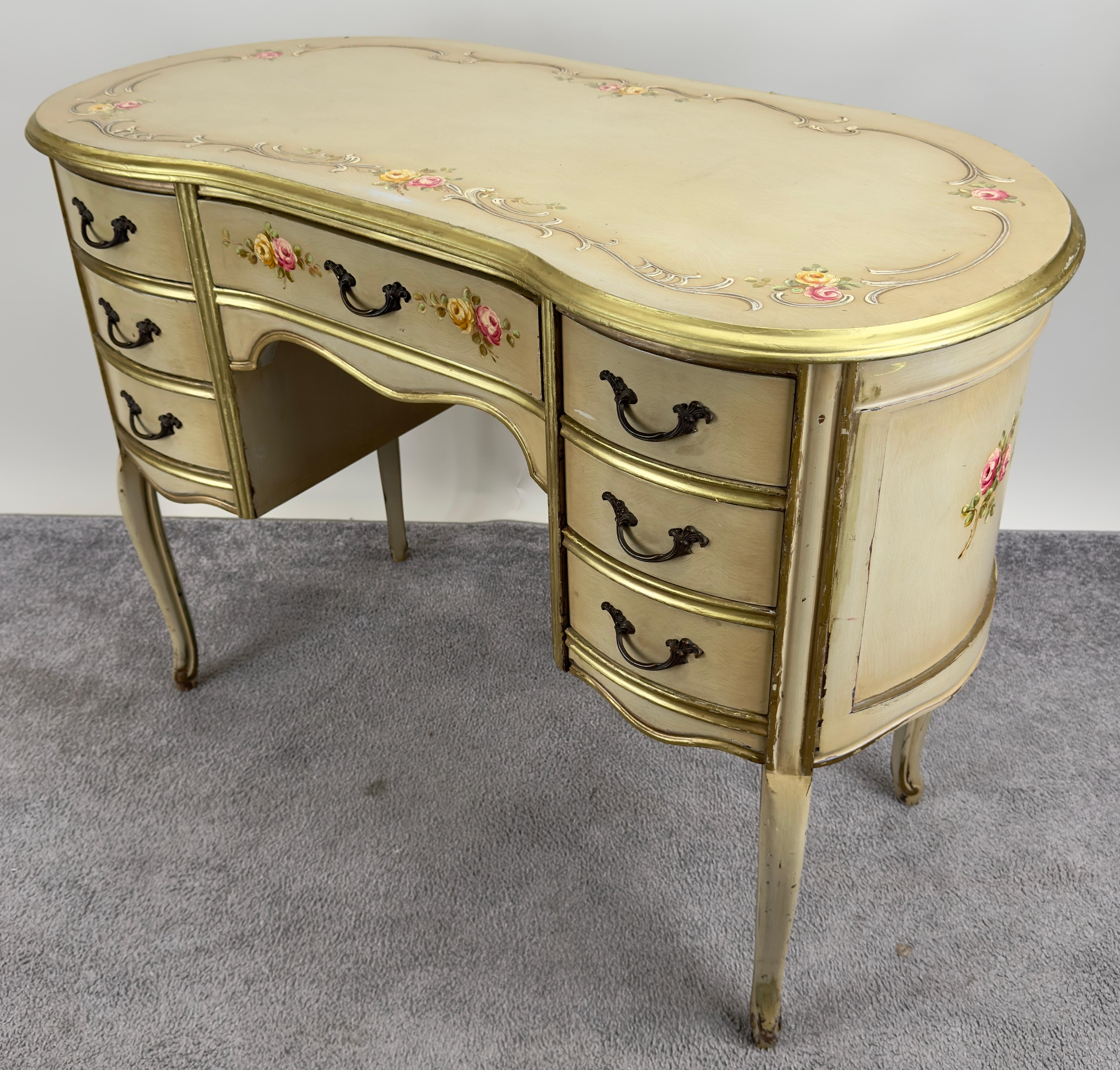 A French Provincial style lady’s writing or vanity desk crafted with a graceful kidney-shaped top, the desk features a cream-colored finish, softened with a delicate patina that speaks to its antique charm. The surface is adorned with hand-painted