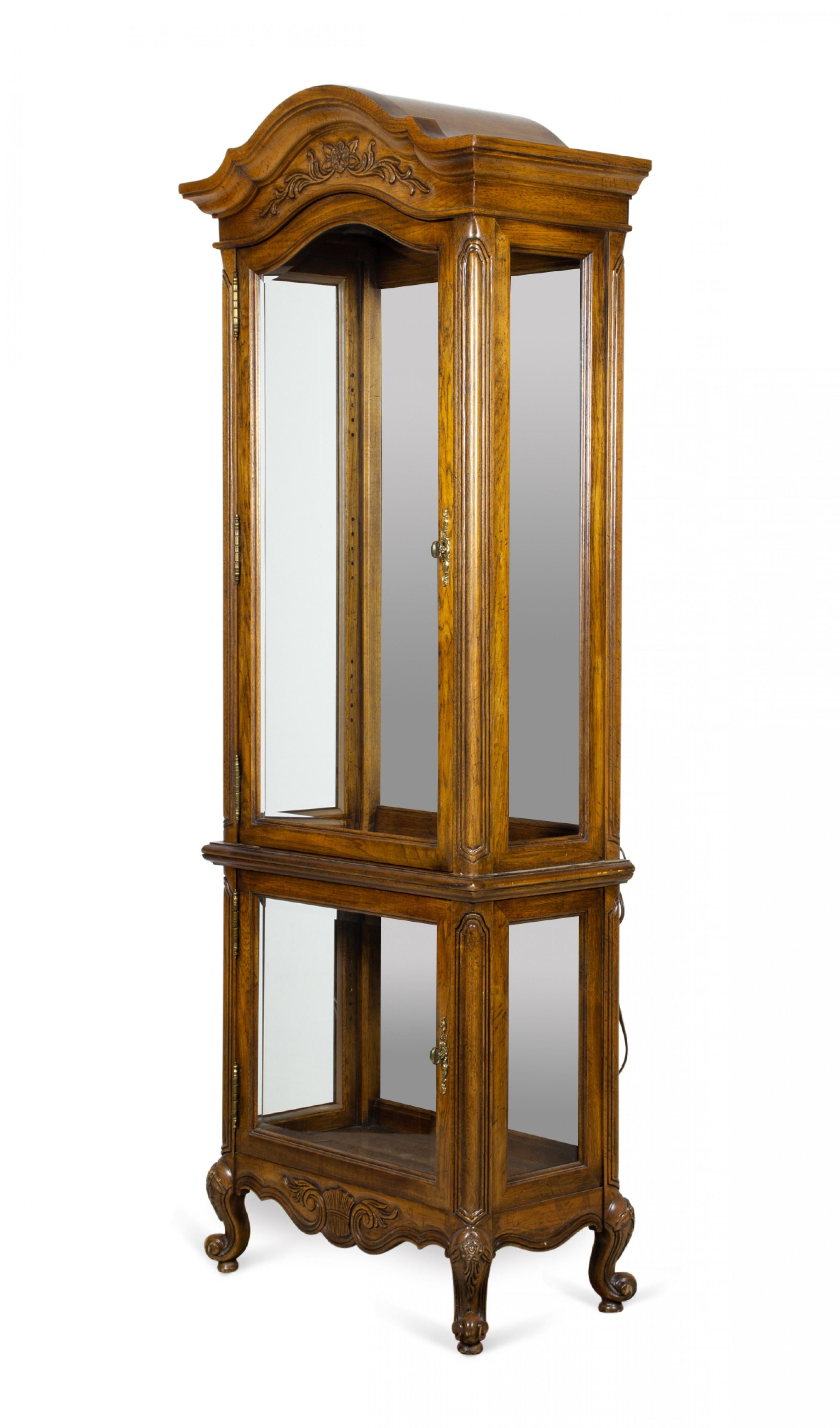 French Provincial-style (20th Century) carved oak display cabinet / vitrine with two display cabinets with mirrored backs and glass doors, wired with internal bulbs, in a carved oak case with shell embellishments and a curved pediment, resting on