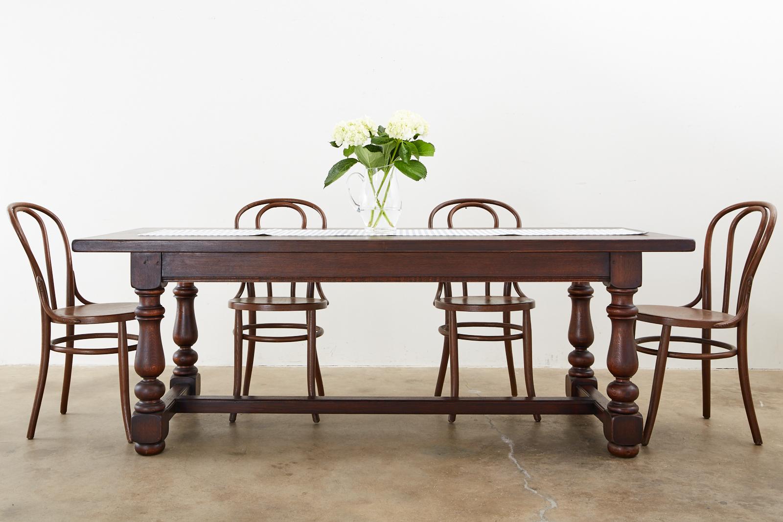 Distinctive French farmhouse trestle dining table made in the provincial style handcrafted from oak. The table features a nearly 2 inch thick plank top supported by a substantial trestle style base. The base has thick, chunky turned legs ending with