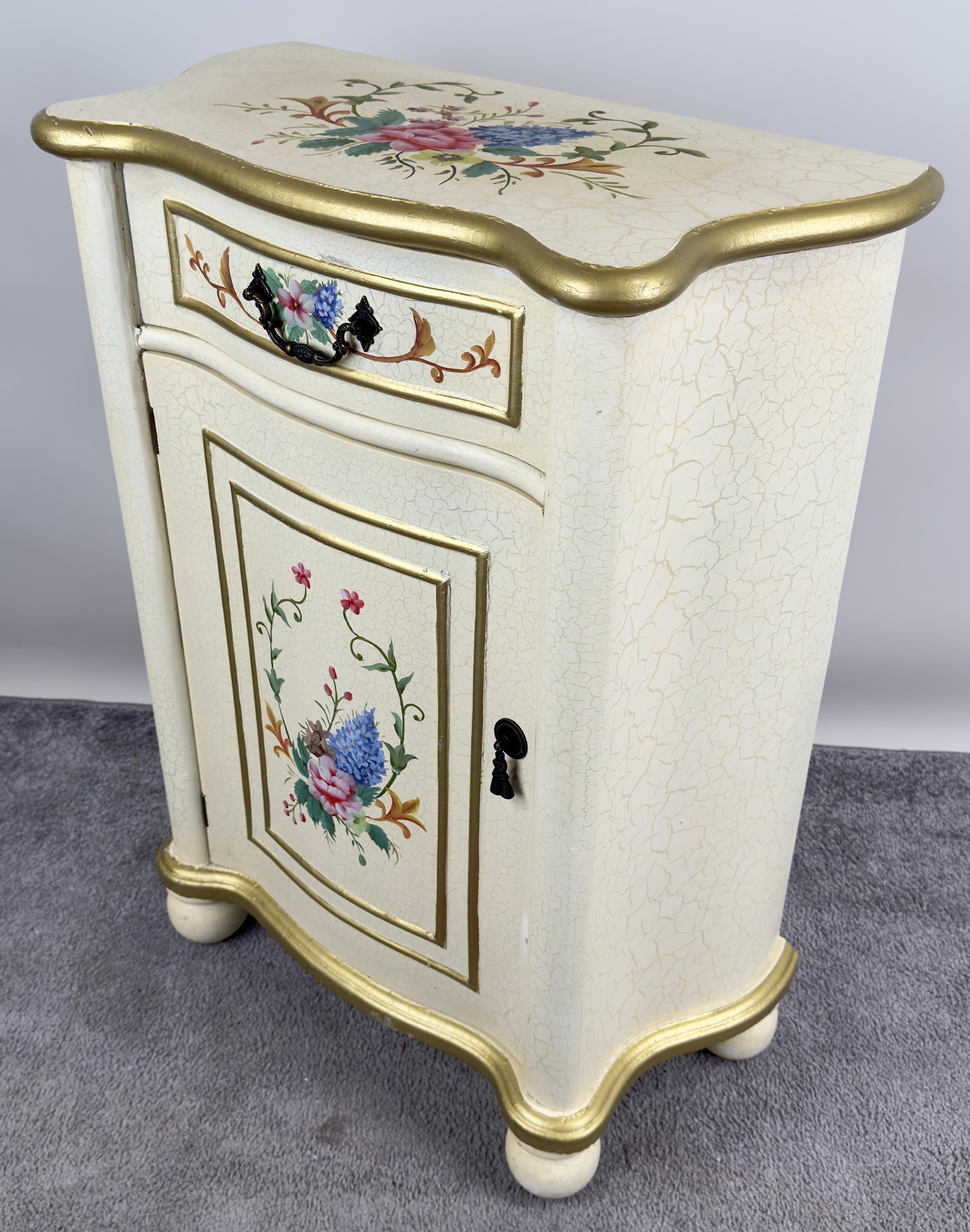 A French Provincial style nightstand , characterized by its graceful curves, delicate details, and hand-painted floral motifs. The piece exudes an air of refinement with its soft cream-colored finish, which has been meticulously accented with a