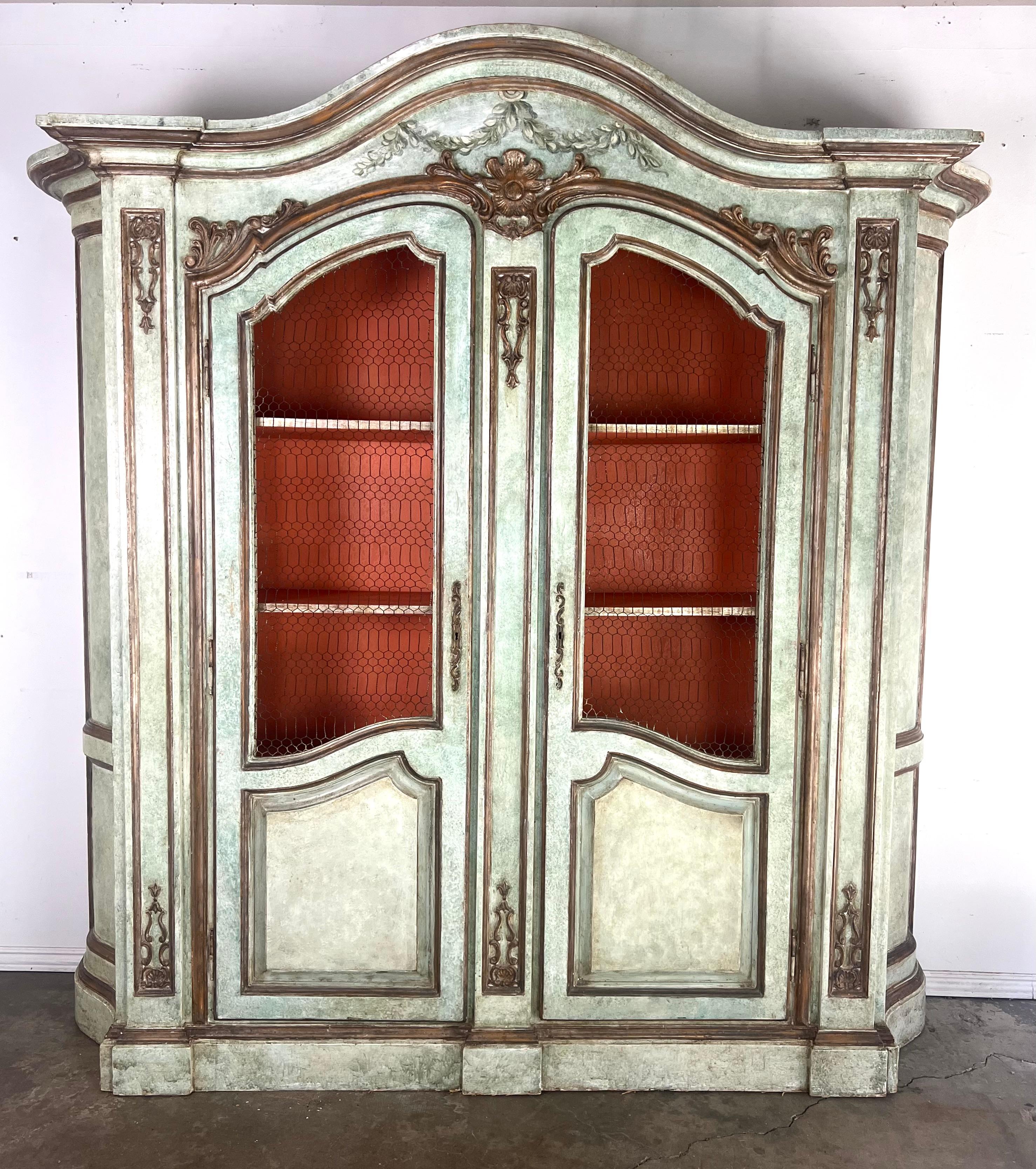 Armario pintado de estilo provincial francés con diseño de doble puerta y parte superior arqueada.  El armario está pintado de color verde claro con reflejos dorados en las tallas.  Las puertas tienen intrincadas tallas florales y volutas.  Estos
