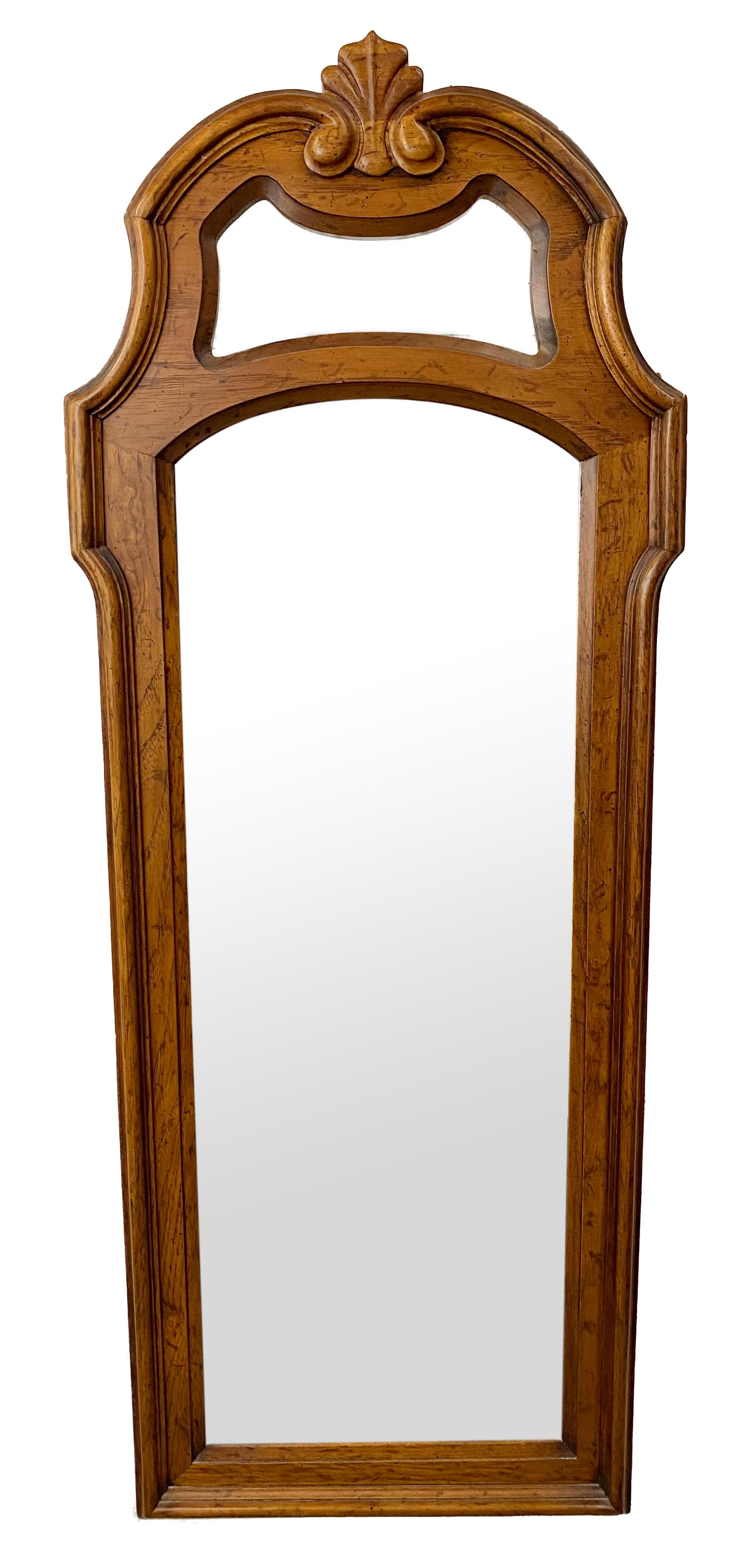A pair of French provincial wall tall mirrors by Drexel Heritage. The quality mirrors 'frame is finely carved of pine wood showing beautiful natural grain. The mirrors are embellished with a large acanthus in the top and feature nice carving