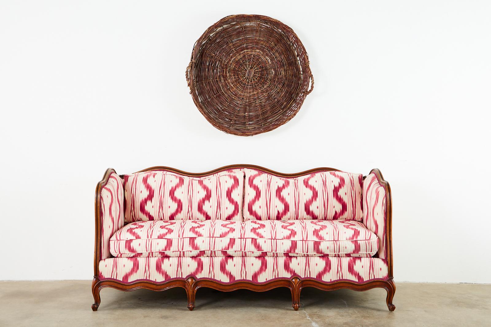 Stunning French Provincial style canape or settee featuring a modern redux with Pierre Frey Toile de Nantes Ikat upholstery. The dramatic hand carved frame has a serpentine back, arms, and apron supported by Louis XV style cabriole legs. The