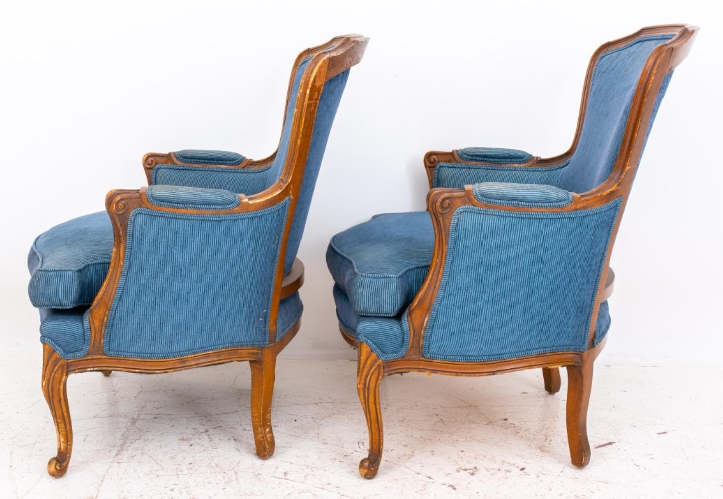 French provincial style upholstered arm chairs or bergeres, with a shaped molded crestrail above an upholstered back en cabriolet, the back, sides, and seat now upholstered in a blue corduroy, on shaped seat above cabriole legs. Measures: 34.5