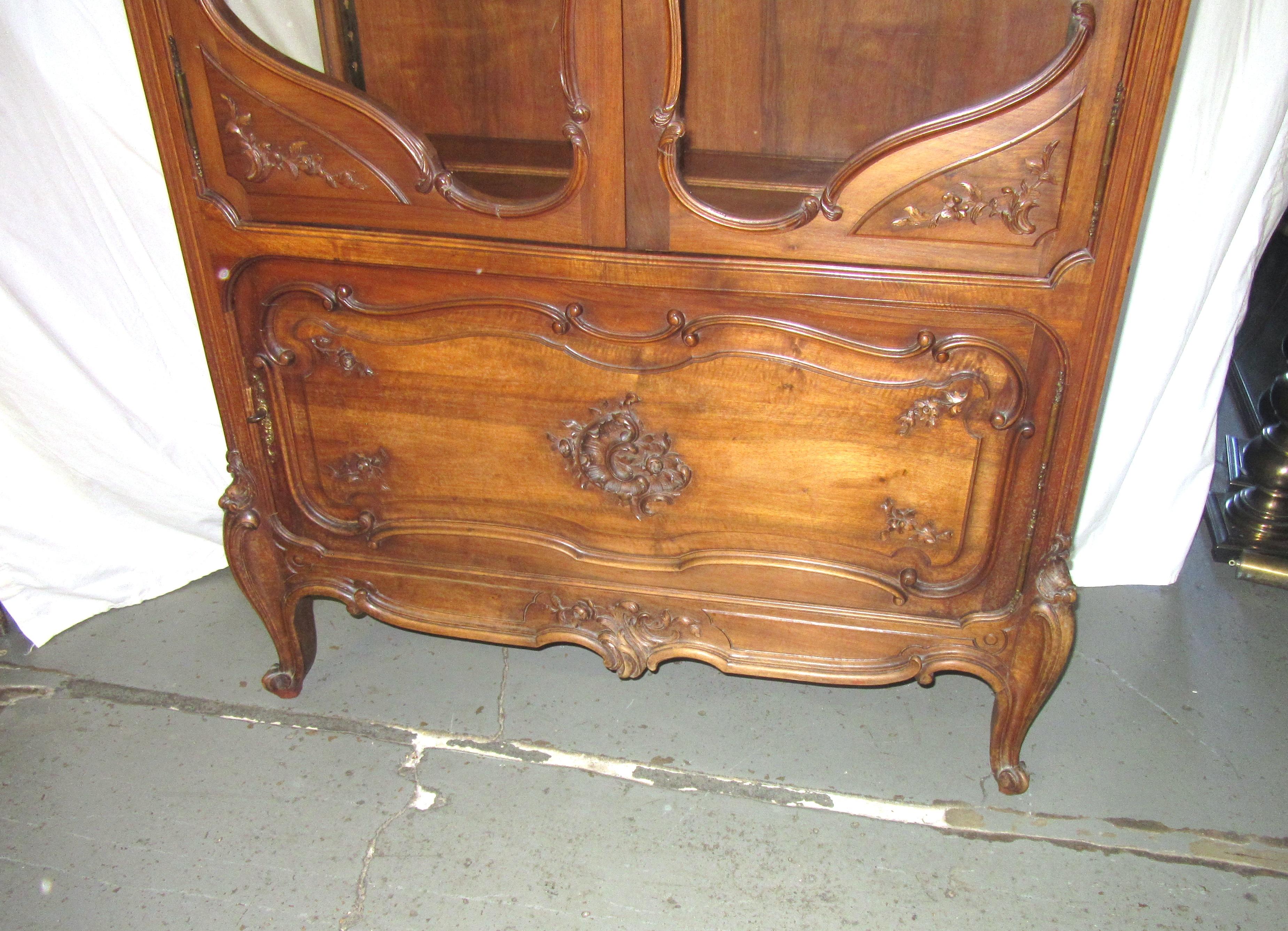 French Provincial style walnut curio cabinet with elaborate carving throughout the piece. Three glass shelves on the inside. Bottom of the cabinet swings out to reveal three shelves where cutlery can be stored. Made in France during the turn of the