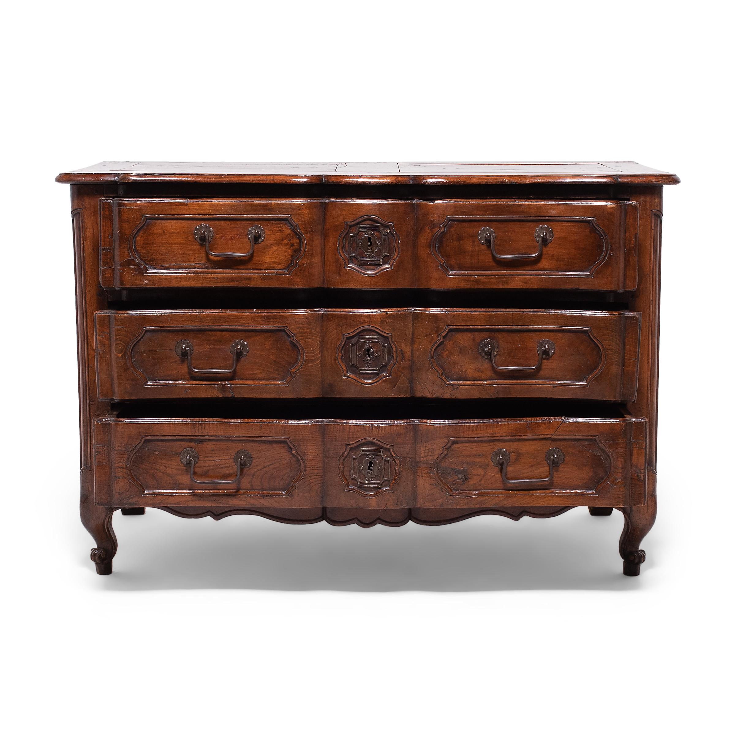 This antique French commode is crafted in the Louis XV Provincial style and dates to the mid- to late-18th century. This example takes its design from early French commodes known as commodes en tombeaux, or chests of drawers, characterized by their