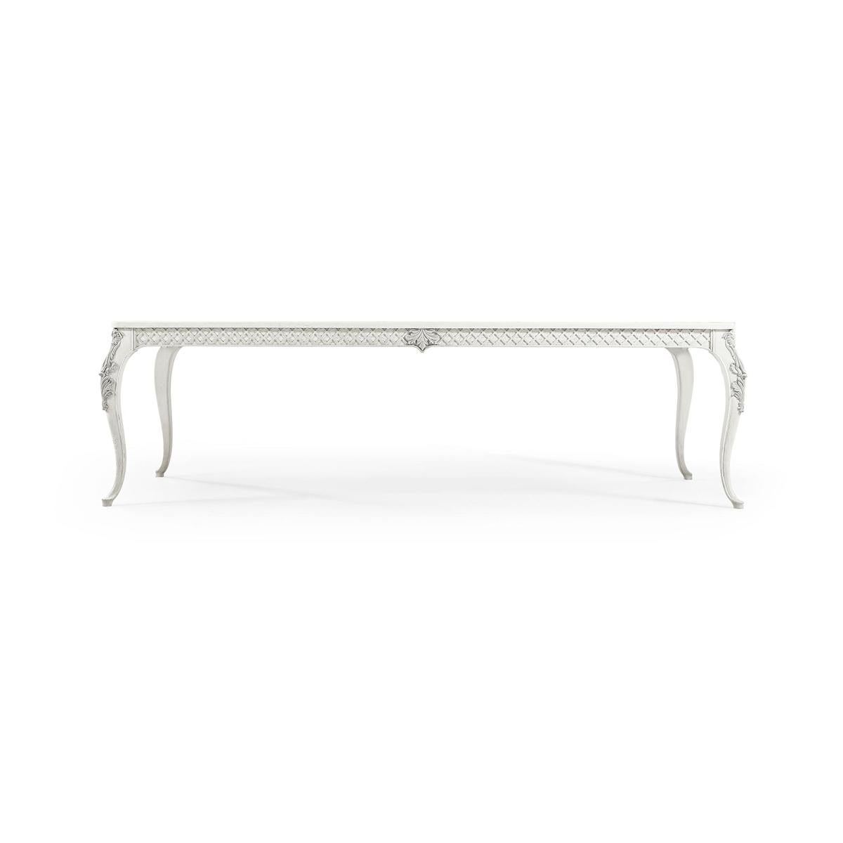 The table is finished in a dry Chalk White with light distressing that adds character and a vintage feel. The legs, sculpted in graceful cabriole style, are adorned with hand-carved floral details and painted in light grey, enhancing their