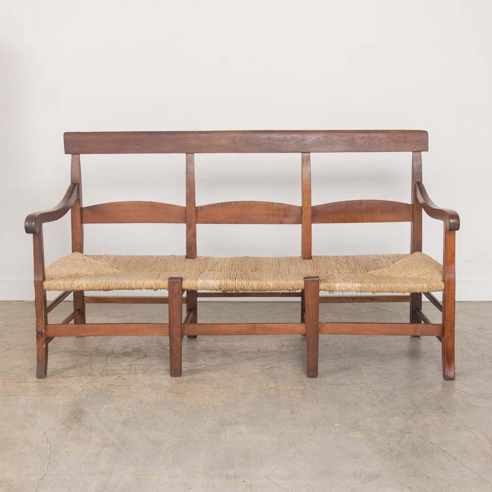 Ravissante banquette provinciale en chêne, France, années 1940. Design simple et intemporel avec une assise en jonc épais tissé et de magnifiques accoudoirs et pieds sculptés avec un dossier en poutre. Le siège en jonc d'origine a été réparé