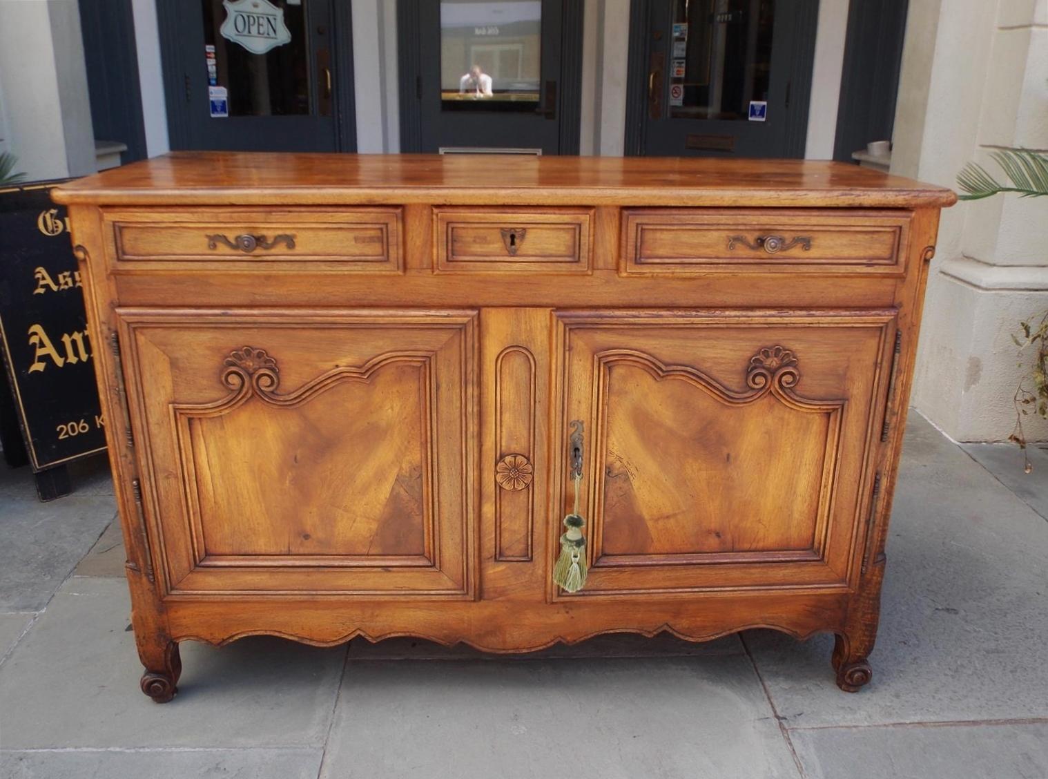 French Provincial cherry server with a carved molded edge top, three upper case drawers with the original hardware, escutcheon, and key, two lower case hinged flanking decorative molded floral doors revealing a centered fitted interior shelf, carved
