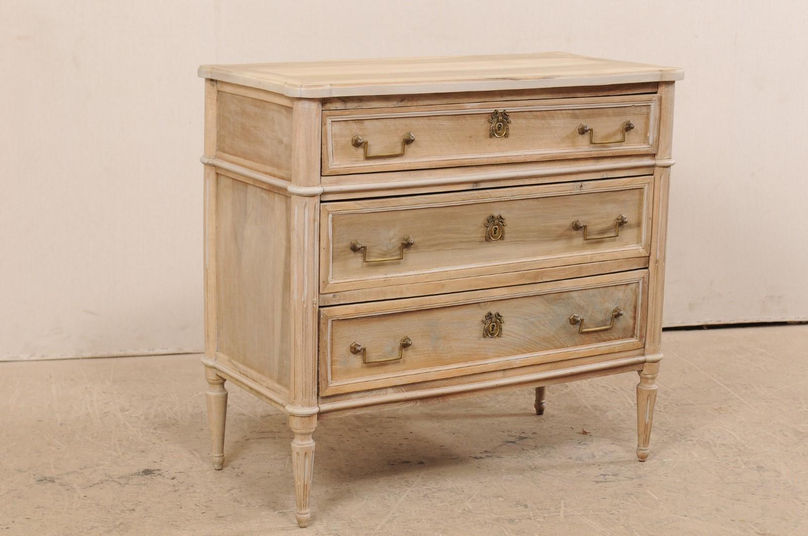 A French chest of drawers from the early 20th century. This antique chest from France features a rectangular-shaped top with pronounced and rounded corners, which rests atop a neoclassical style case with rounded and fluted front and back side