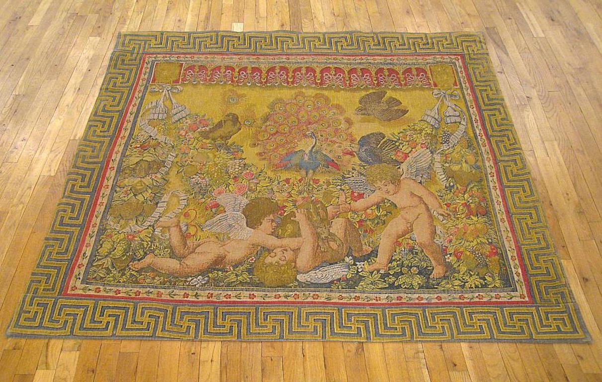 A French Rambouillet pictorial tapestry from circa 1890, portraying a trio of putti at play in a paradisiacal floral setting, with peacocks and other birds in the background, within an interconnecting key design border. This is a replica from a set