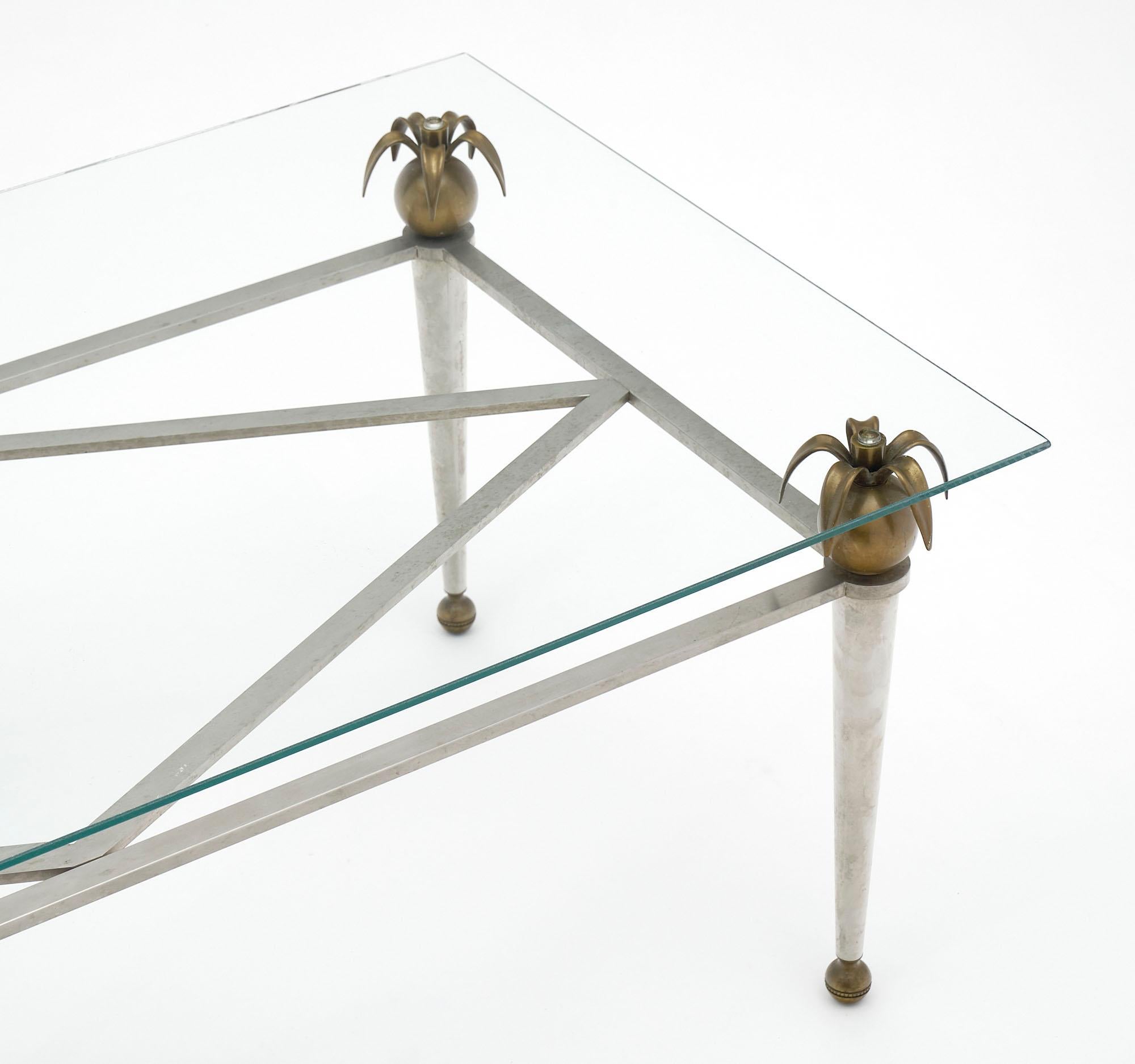 Table basse de France en acier et laiton. Les quatre sphères avec palmes maintiennent le plateau en verre transparent.
