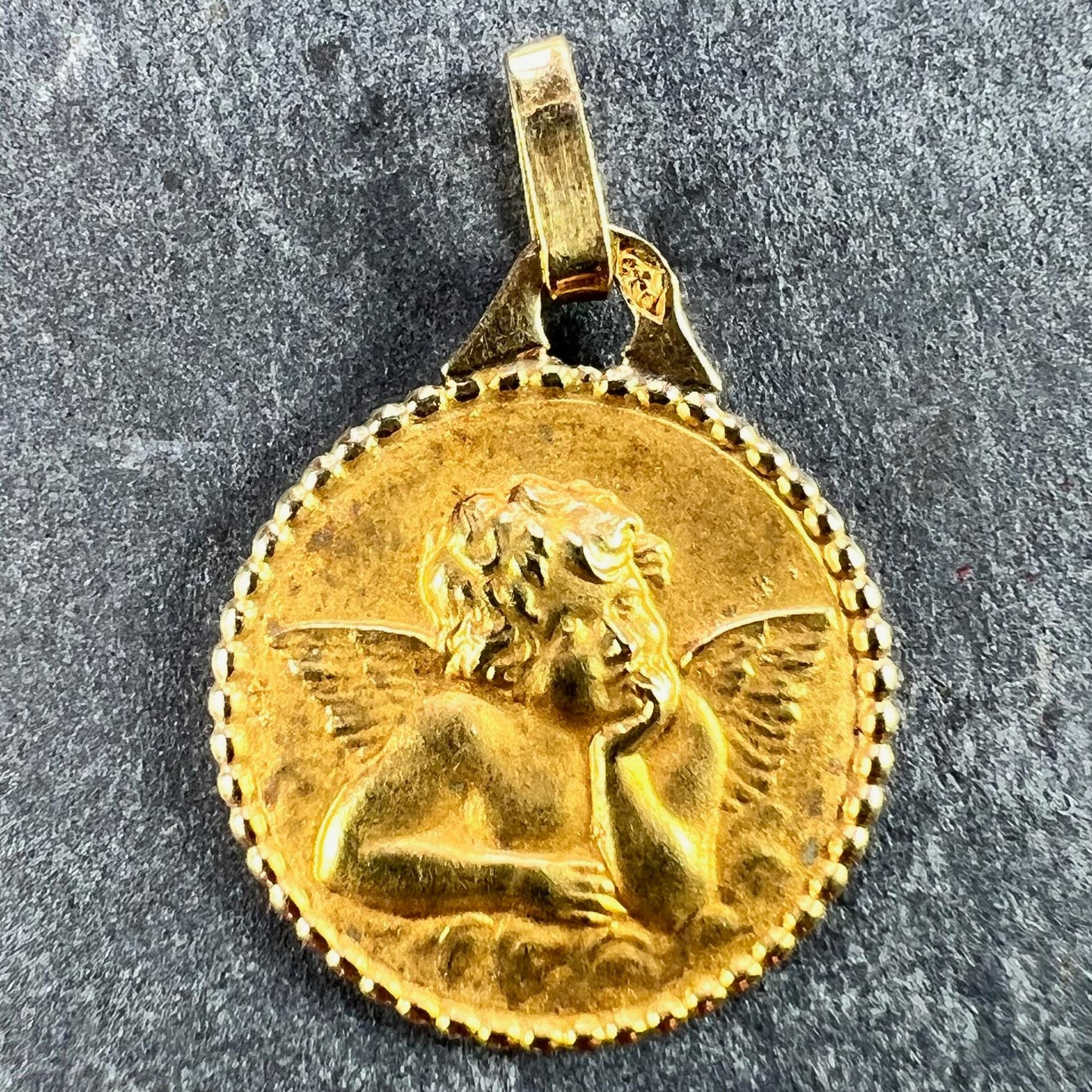 A French 18 karat (18K) yellow gold charm pendant designed as a round medal depicting Raphael’s cherub. The reverse with a bell surrounded by cherubs. Stamped with the eagle mark for 18 karat gold and French manufacture with an unknown maker's