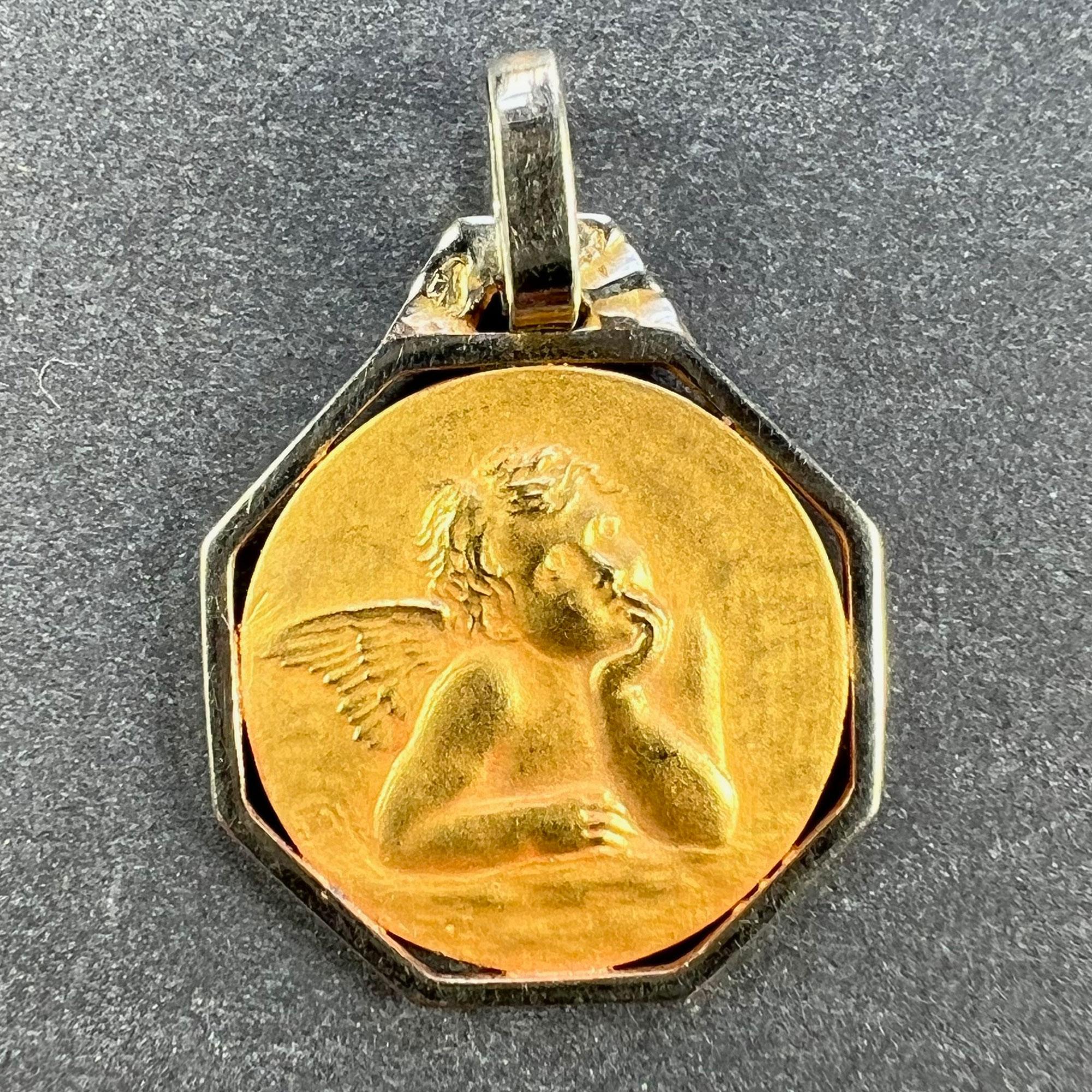 A French 18 karat (18K) yellow gold charm pendant designed as a circular medal depicting Raphael’s cherub within an octagonal white gold frame. The reverse shows a relief of wedding bells. Stamped with the eagle mark for 18 karat gold and French