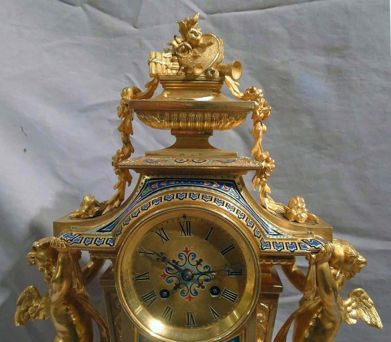 French antique, rare Champleve enamel and ormolu mantel clock. A very rare model with two good figures of cupids holding up the platform on which the clock face rests and the swags and urn holding musical trophies is held by. Profusely decorated