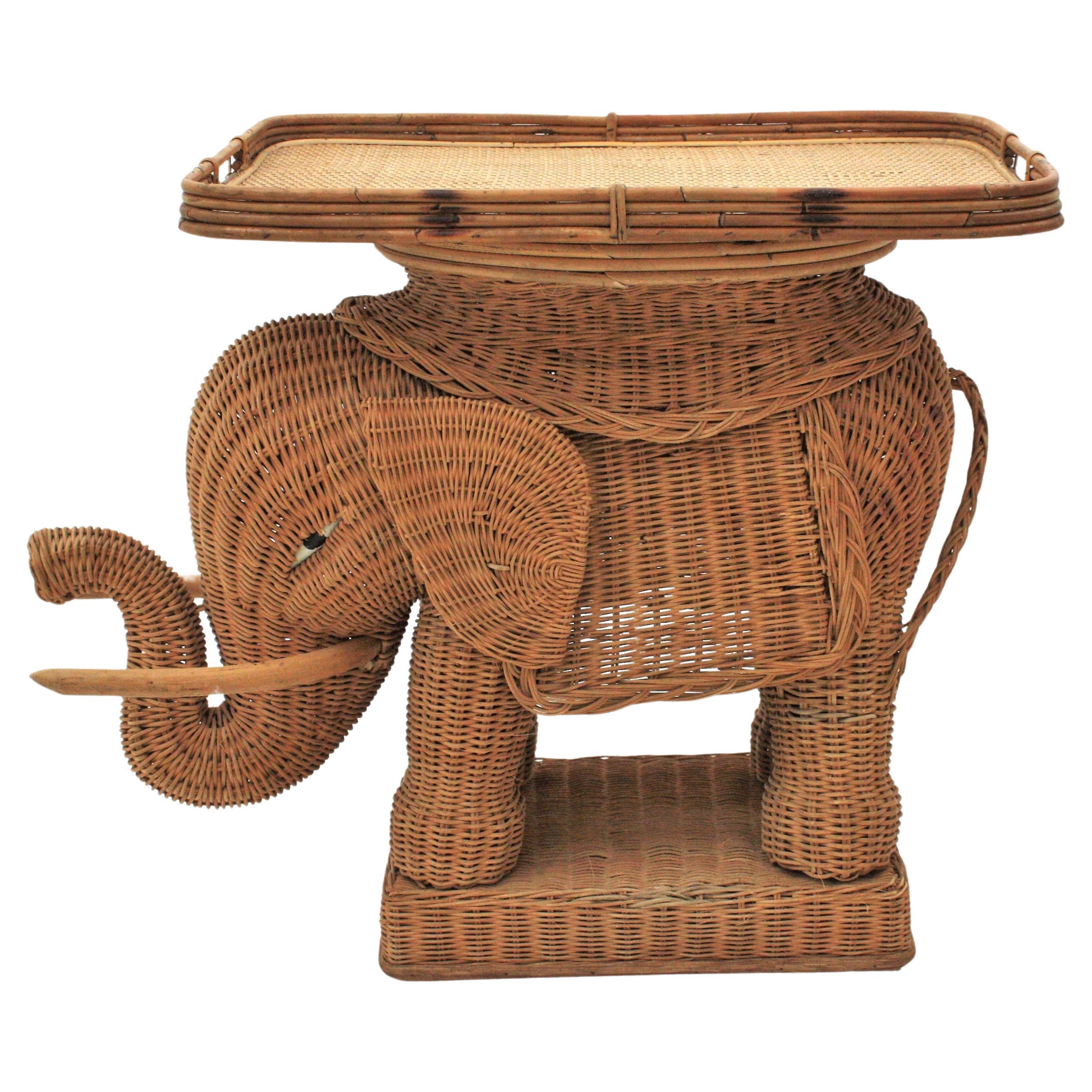 Eye-catching woven rattan end table or drinks table with removable tray top. France, 1940s-1950s.
This elephant shaped end table stand was beautifully constructed in hand braided rattan / wicker accented with wood tusks. The rectangular tray top is
