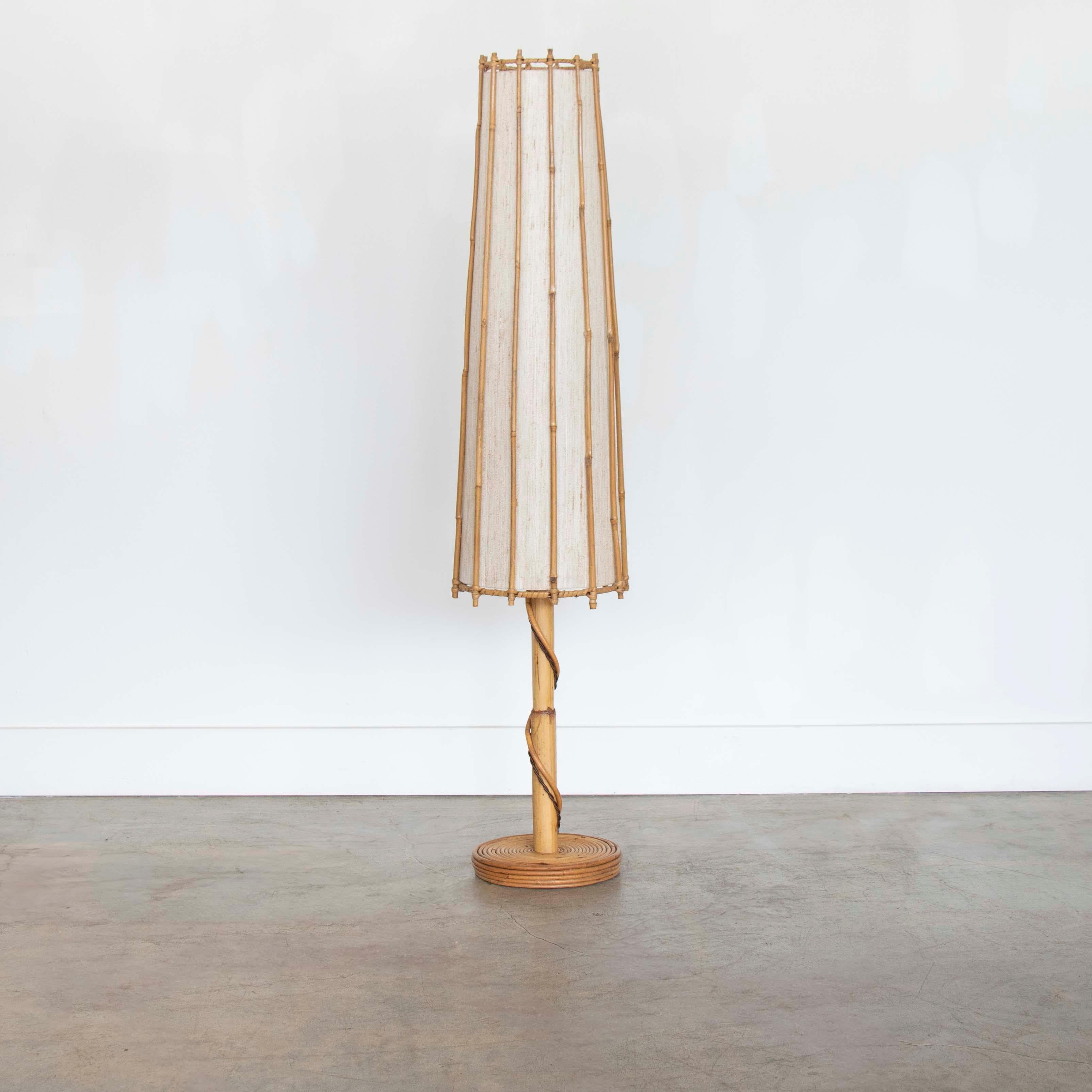 Beautiful rattan floor lamp in the style of Louis Sognot from France, 1960's. Circular rattan base and stem with large tapered rattan shade. Original linen interior shade lining and rattan show great age and patina. Newly re-wired. Takes one E26