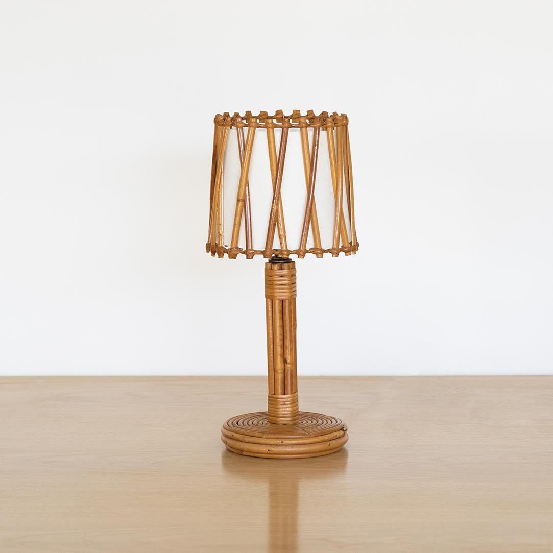 French rattan table lamp in the style of Louis Sognot. Circular base and stem with rattan drum shade, crisscross rattan detail and silk interior shade lining. Newly rewired. 



 