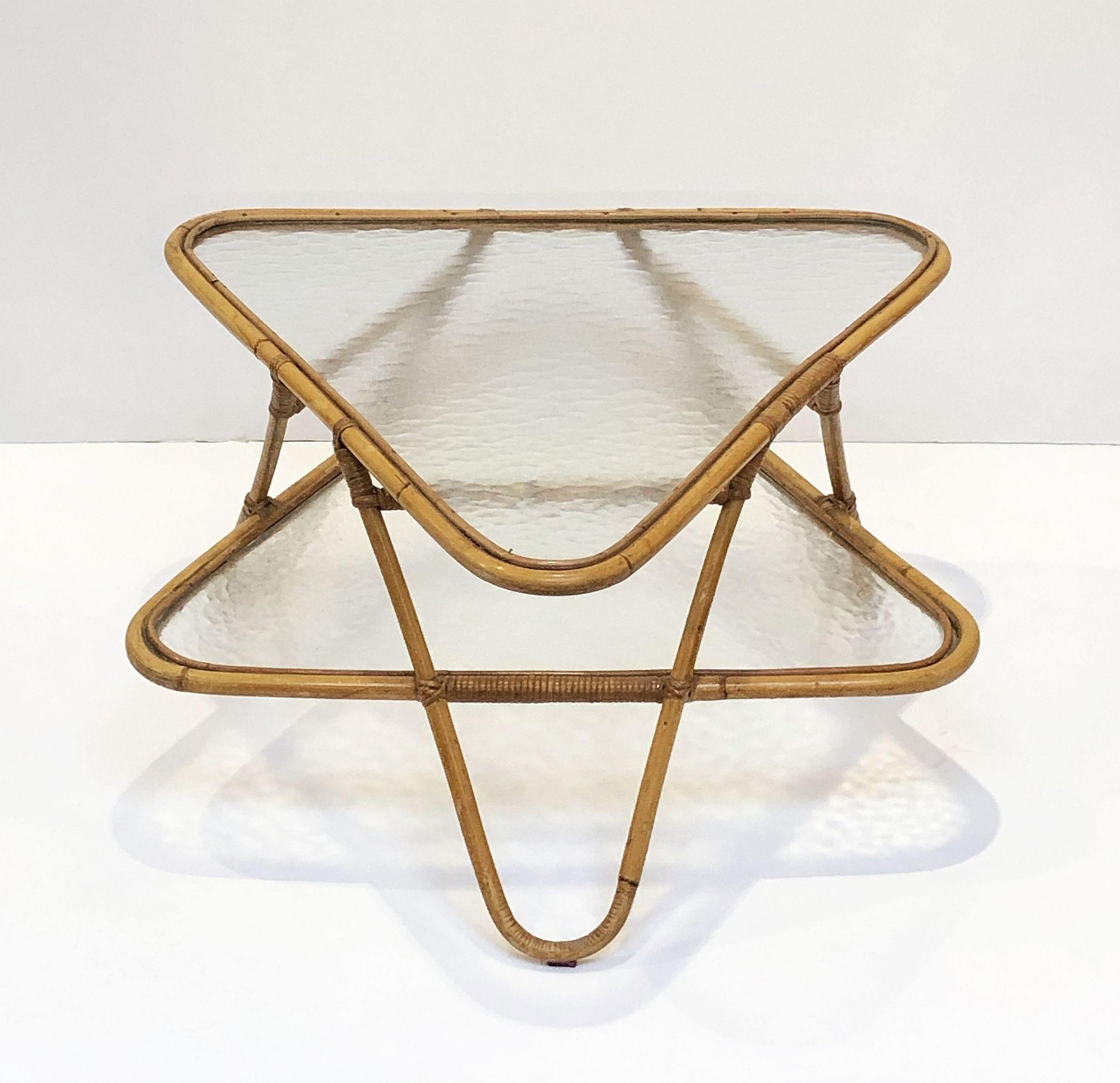 A fine French handcrafted midcentury rattan and bamboo low cocktail or coffee table.
Featuring a two-tiered body of two inverted glass triangles with decorative cane bamboo accents, the top tier with rounded corners over a bottom tier with three