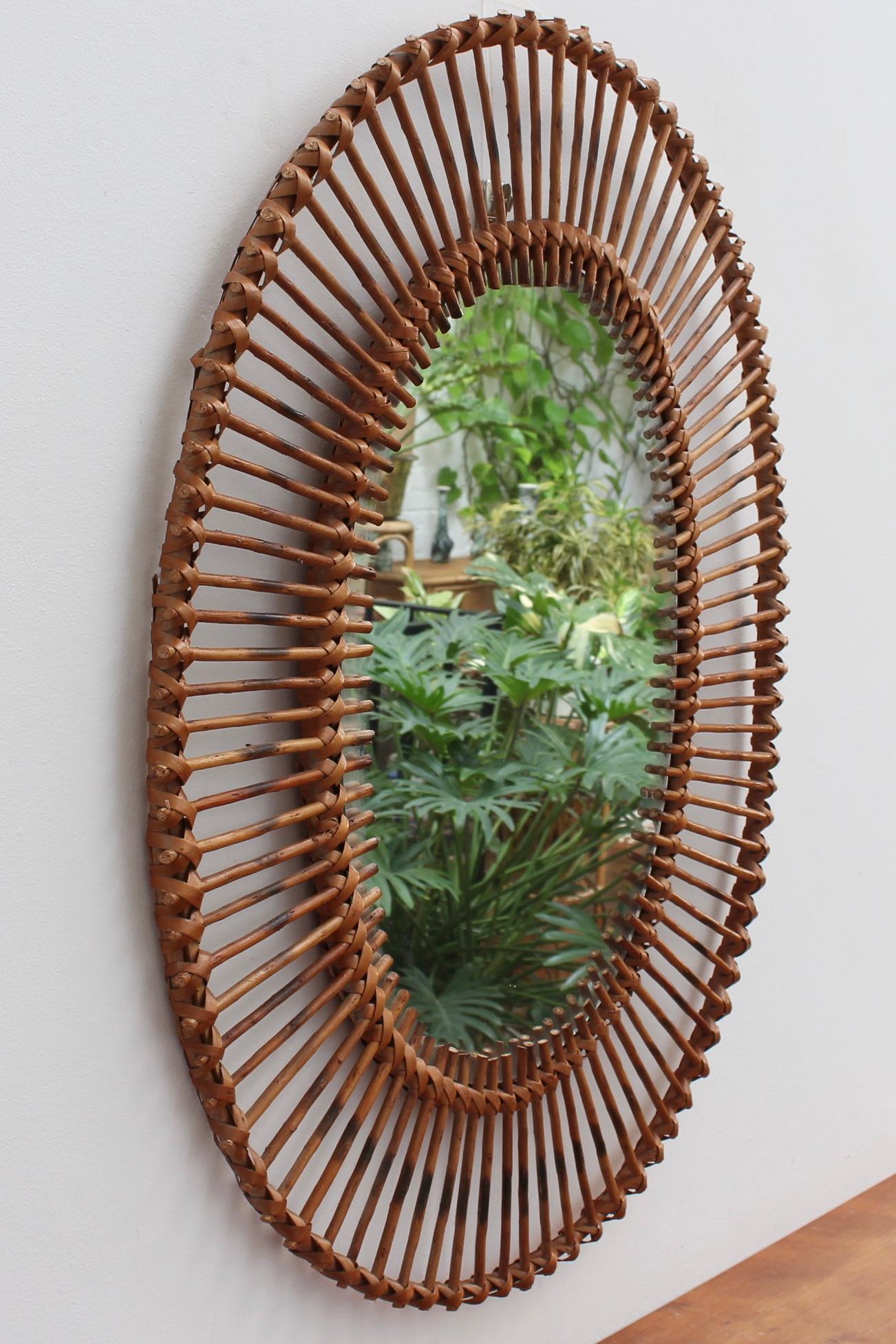 French rattan oval-shaped wall mirror (circa 1960s). A distinctive vintage mirror which transports you immediately to another place and another time, perhaps the French Riviera or Miami's South Beach, circa 1960. Its elegant glass is oval-shaped,