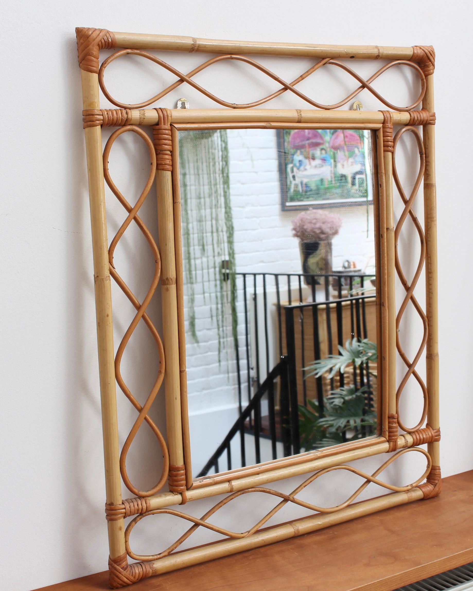 French rattan wall mirror (circa 1960s). This is an Asian-inspired design with inner and outer frames connected by figure-eight shapes of rattan cane. The corners are lashed together and protected with rattan strands. Incredibly stylish, it can add