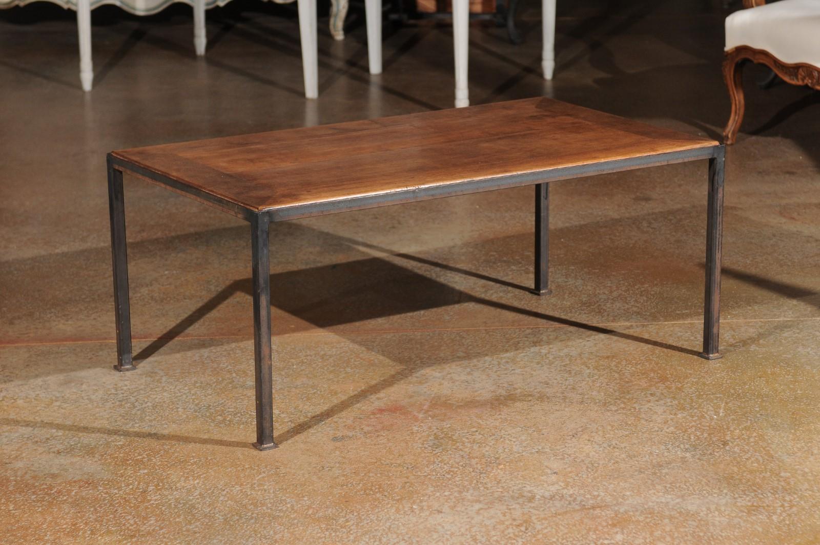 A French coffee table made from old walnut and raised on an iron base. With its clean lines and contrasting colors, this coffee table will bring a stylish presence to any home. Presenting a rectangular planked top boasting a lovely patina, the table