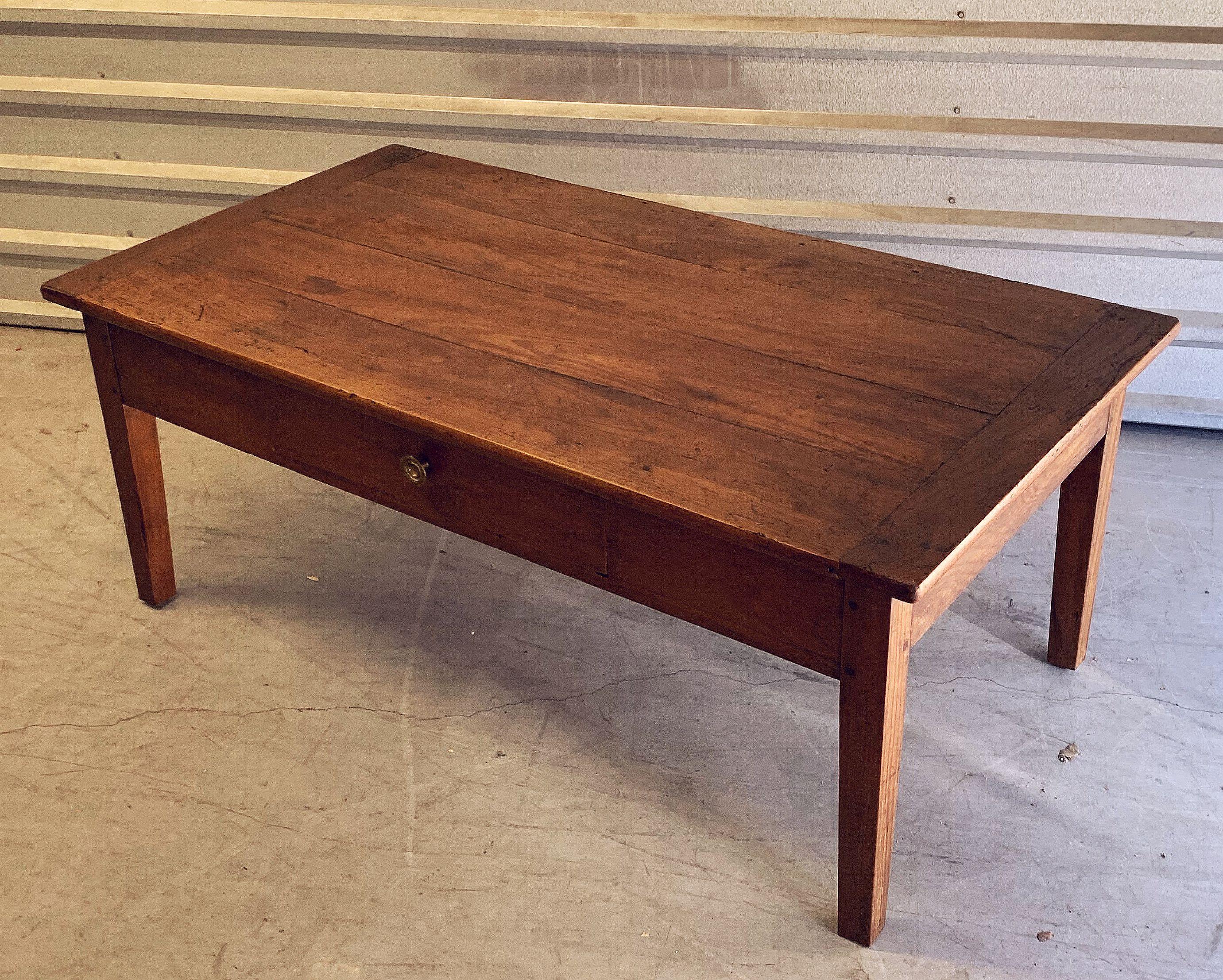 A large French cocktail or coffee (low) table of finely patinated cherry wood, featuring a handsome rectangular plank top set upon a frame of four pegged and tapered legs and one facing drawer with brass knob pull.

The whole with a fine patina,