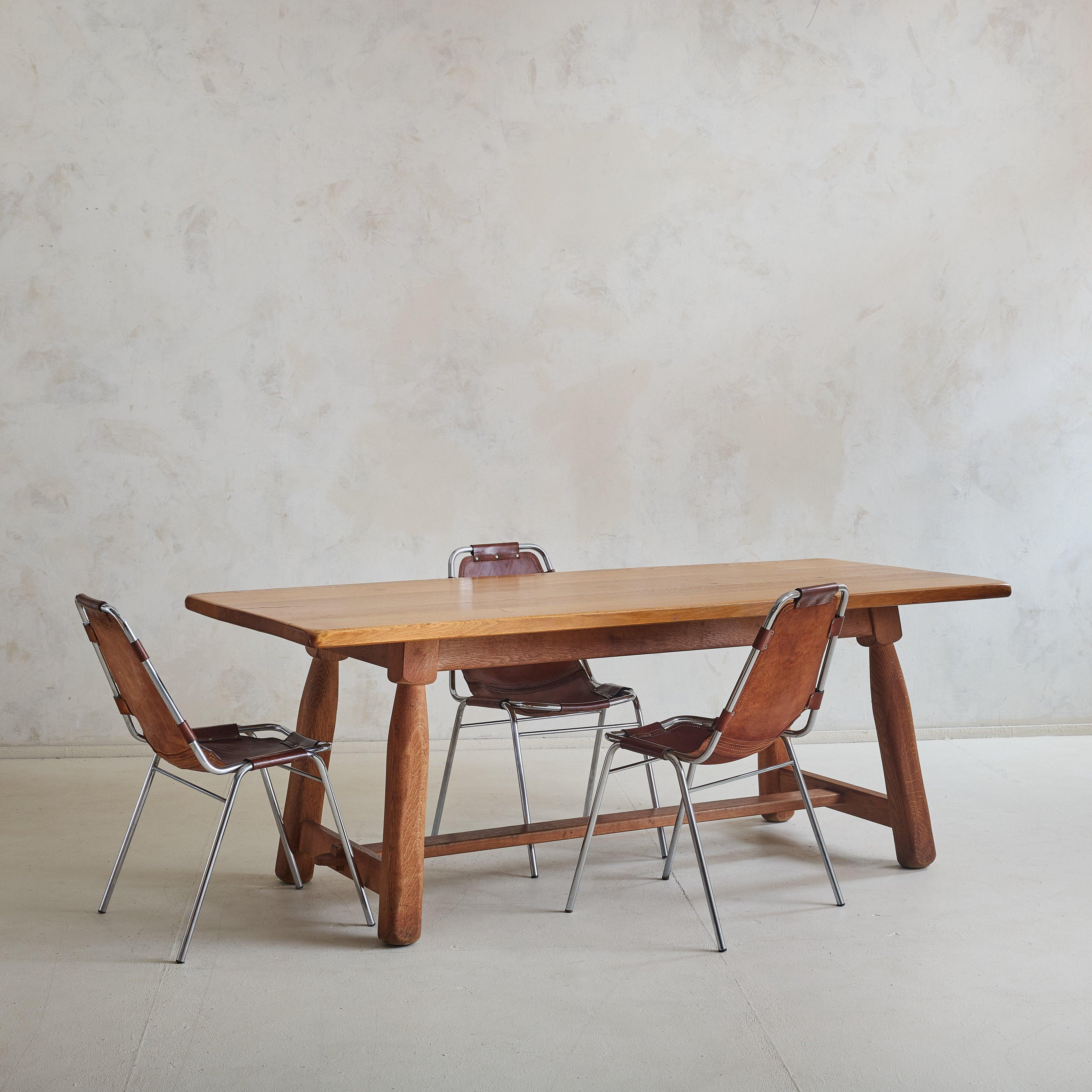 A simple yet refined 1960s French dining table, crafted entirely from solid oak with a commanding presence. The thick tabletop features smooth, rounded edges that reveal the rich, natural grain of the wood. Sturdy, slightly tapered legs anchor the