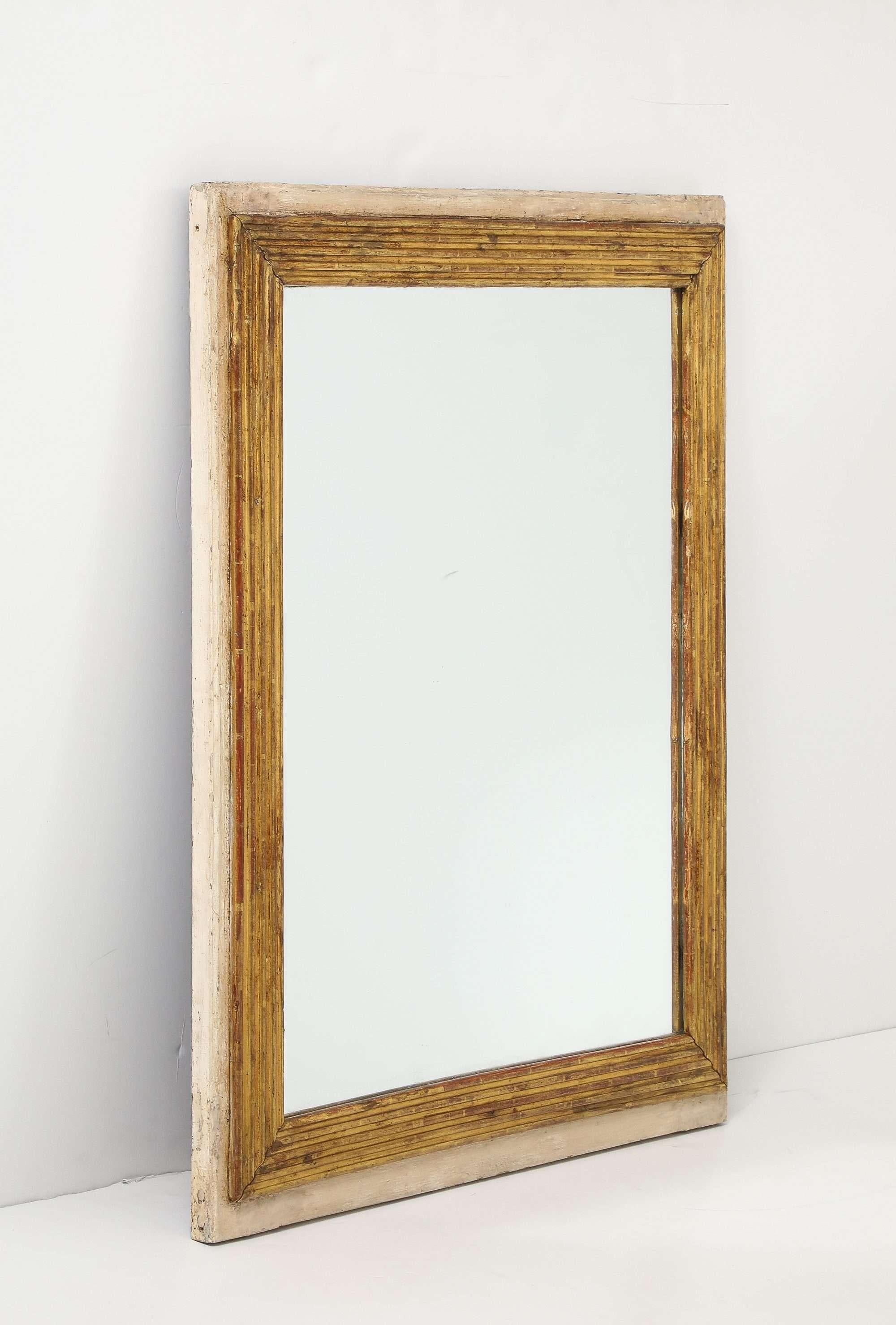 Espejo rectangular de estilo Luis XVI, con marco interior de madera dorada, finamente acanalado y rodeado de un suave borde crema desgastado por el tiempo. Esta pieza tiene una discreta elegancia atemporal y combinaría bien tanto en un espacio