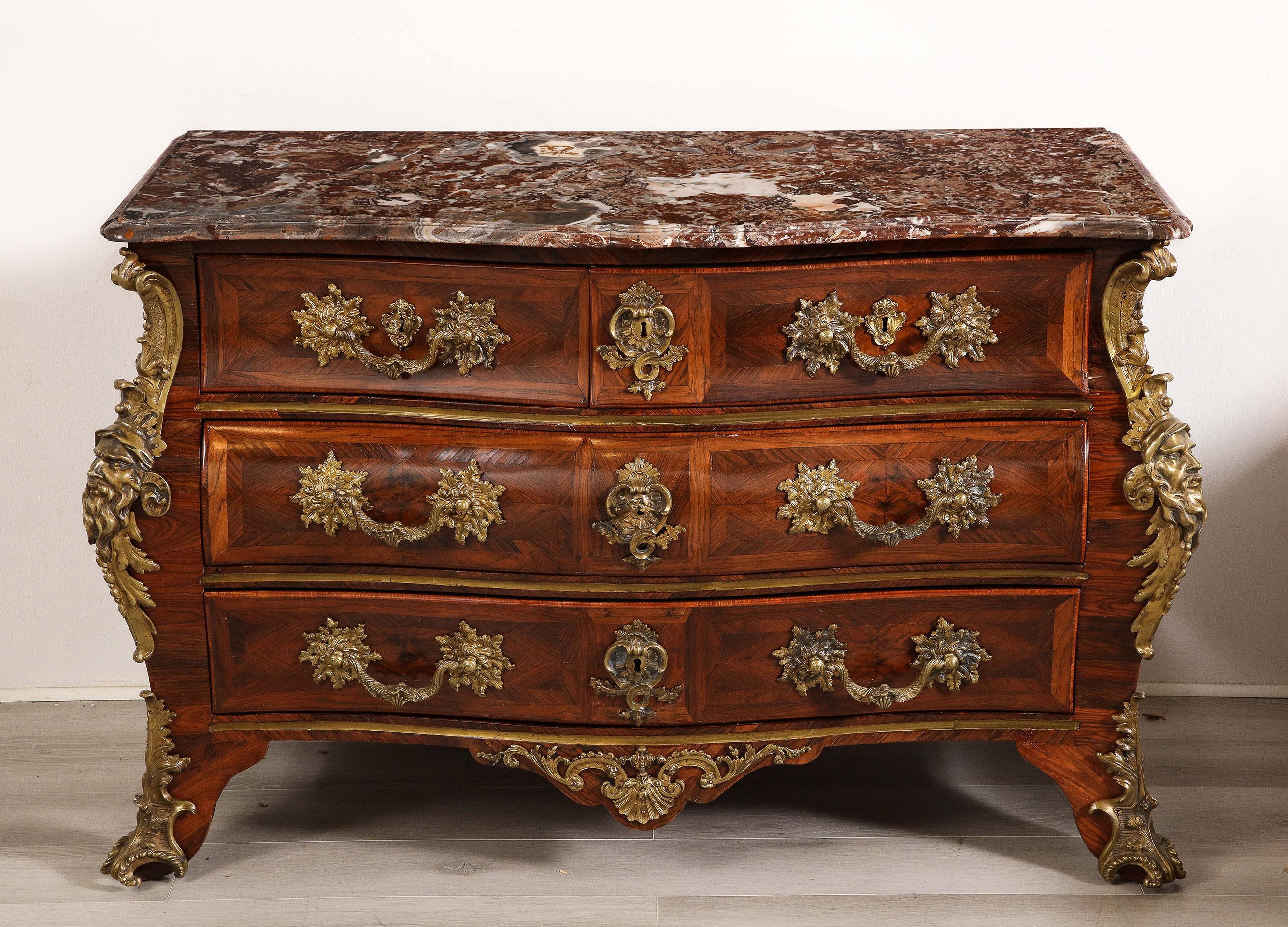 The shaped brèche d'Alep marble top, above a bombé form body with two short and two long drawers spaced with brass insets and with bronze pulls, the corners mounted with bronze Grecian mask escutcheons, on short cabriole legs. 
Stamped M. Criaere.