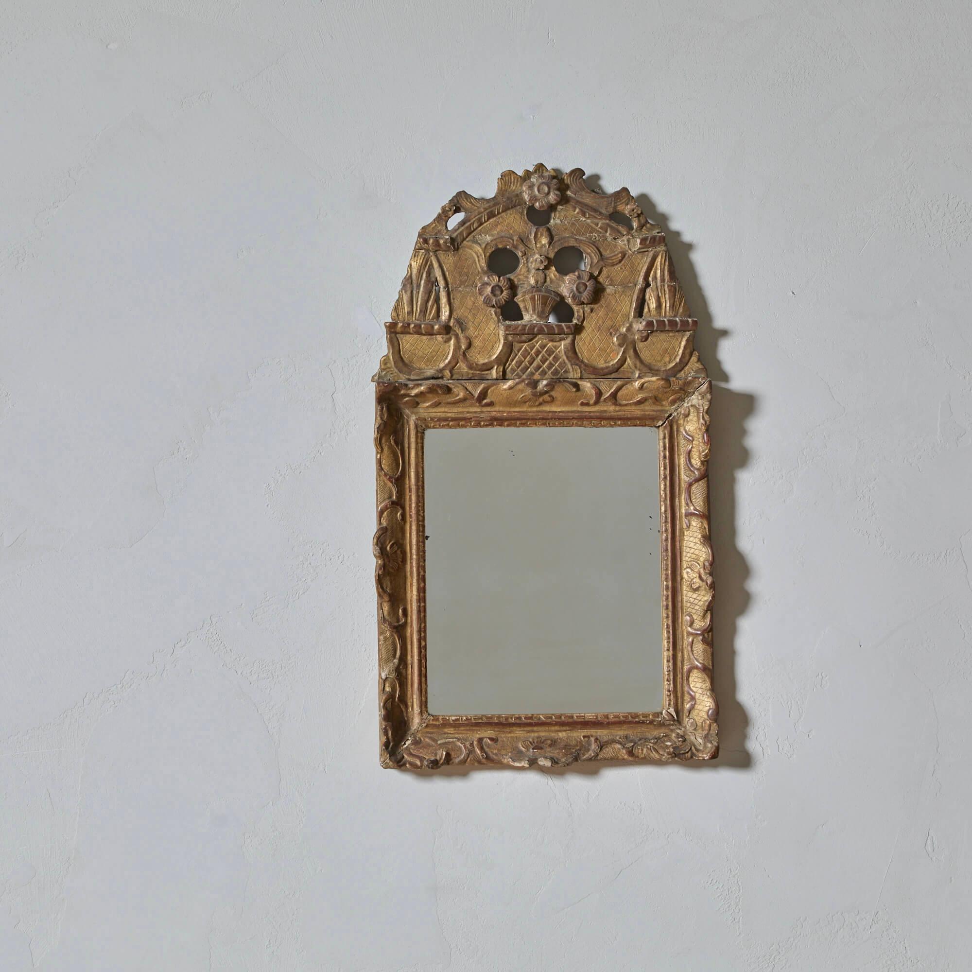 Encantador espejo de madera dorada con superficie bien envejecida, el alto frontón adornado con flores y un motivo de rombos grabados.

