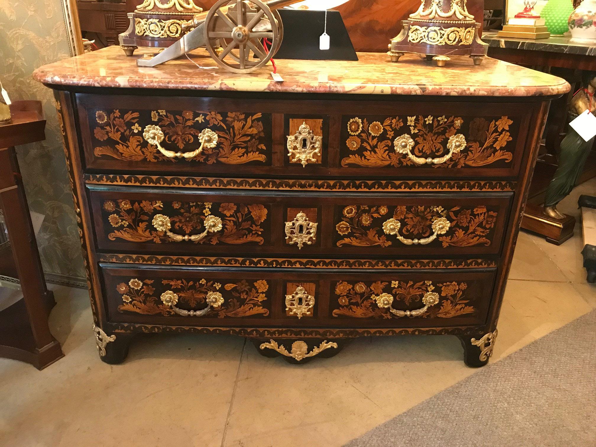 This sumptuous commode once stood in the entrance to a Montreal mansion. Enclosed by three graduated drawers, the front and curved sides are profusely inlaid with panels of floral marquetry. The bronze bail handles are cast and gilt. The beveled