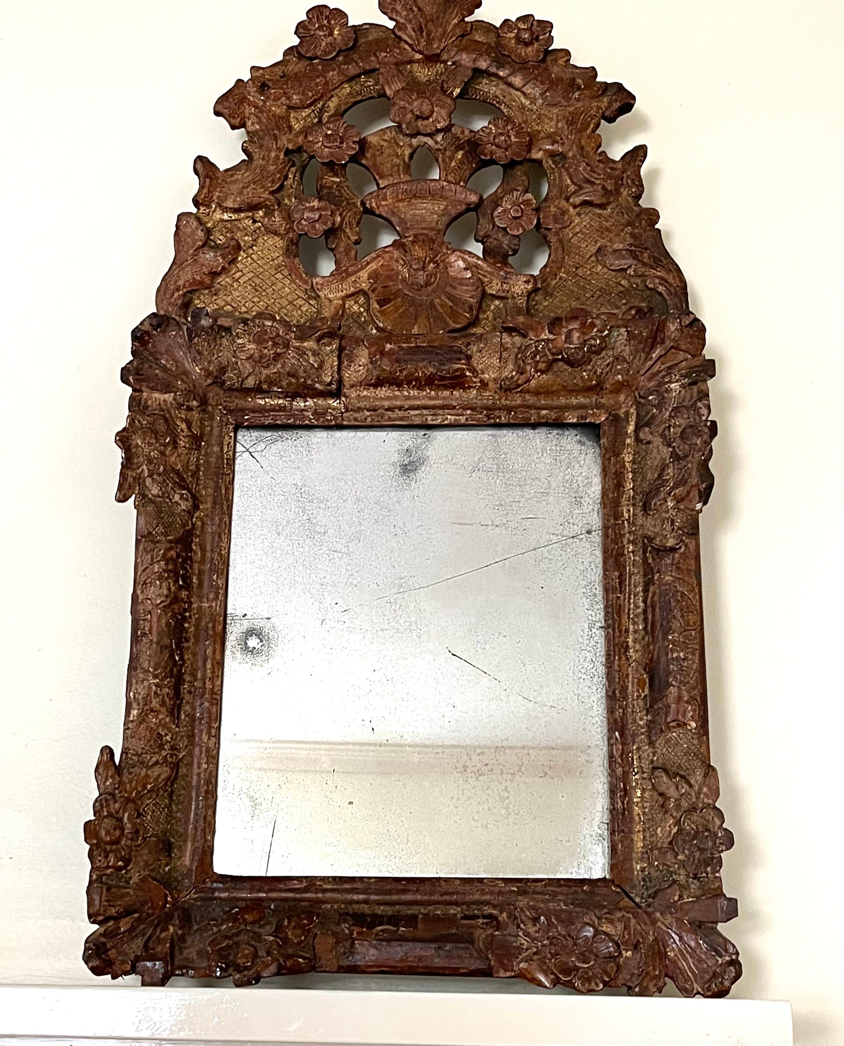 An early 18th century Regence period giltwood framed mirror with upper crest depicting a basket of flowers over a scallop shell with other rocaille decoration. It retains its original mercury glass plate with expected wear and hazing to the glass.