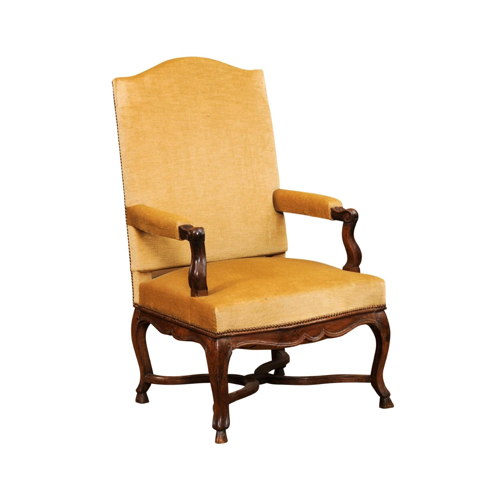 A large French Régence style walnut fauteuil circa 1790 with tall slanted back, open arms with scrolling knuckles, scalloped apron, cabriole legs, hoof feet and curving X-Form stretcher. Immerse yourself in historical elegance with this French