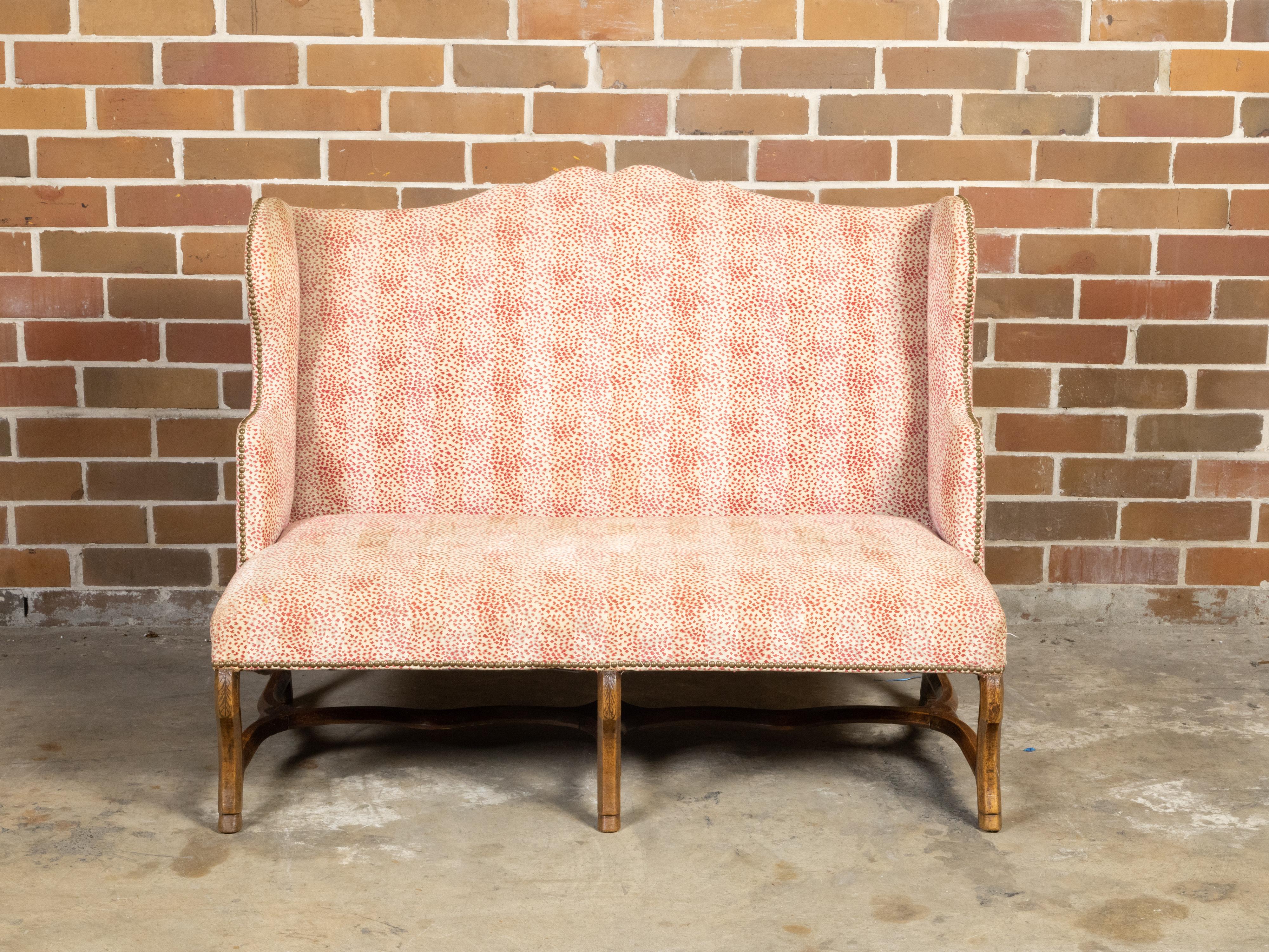 A French Régence style wingback sofa from the early 19th century, with cabriole legs, cross stretcher and red and white blotched upholstery. Created in France during the early years of the 19th century, this 
