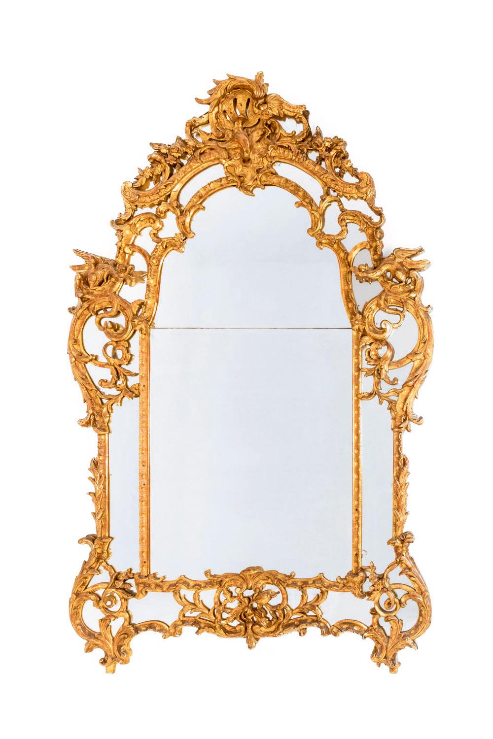 Large glazing beads French Regence style giltwood mirror. General rectangular shape with mirror glass edges in a chantourné shape standing on two short legs. Upper corners richly adorned with molding frames decorated in the Bérain style with two