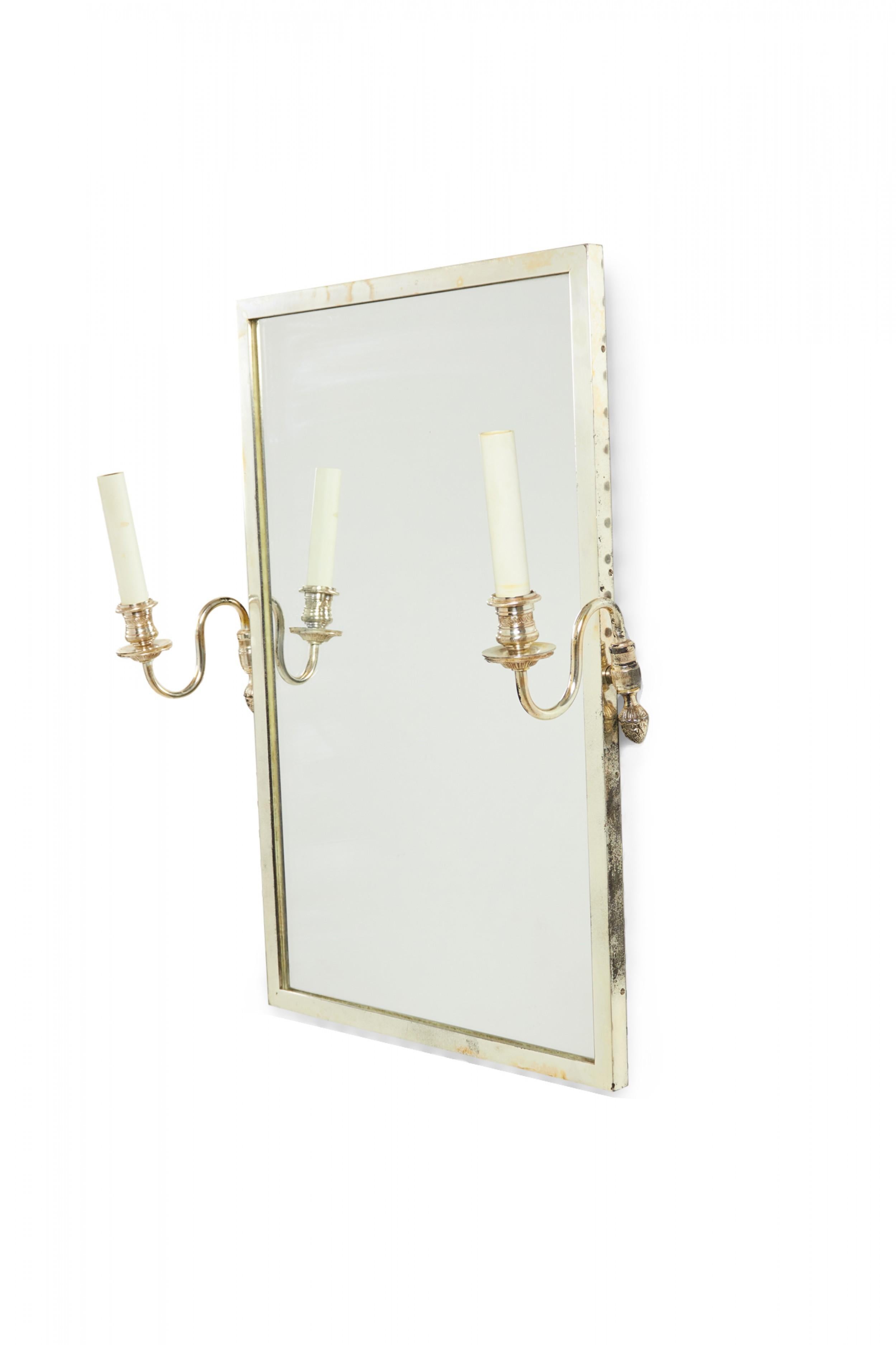 Specchio da parete rettangolare incorniciato d'argento in stile Regence francese con due bracci elettrificati d'argento a forma di applique con manicotti per candele in plastica bianca su entrambi i lati.

La cornice è appannata, un braccio