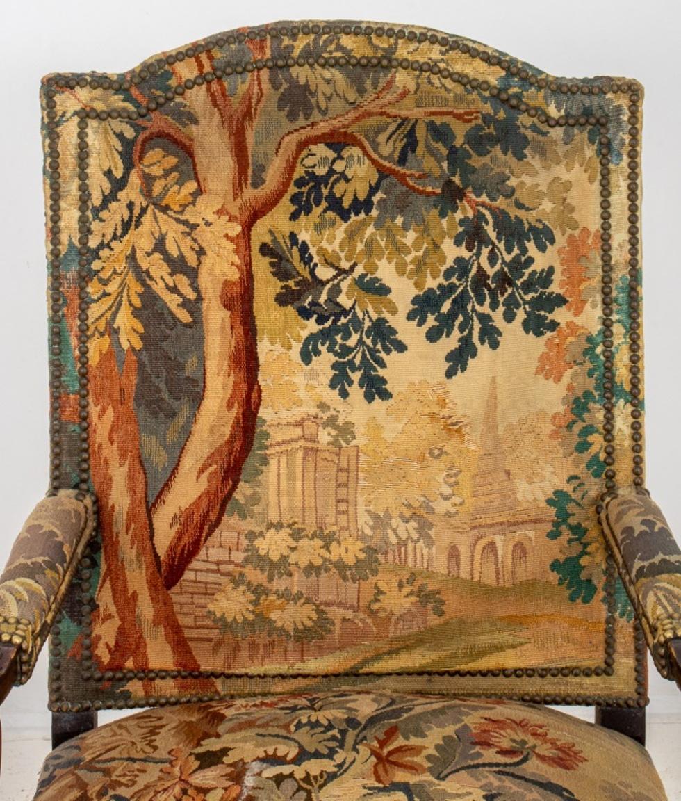 French Regence Style tapestry and nail-head upholstered arm chair or fauteuil a la reine, with shaped rectangular back issuing scrolling arms with foliate relief, the shaped square seatrail similarly carved above four cabriole legs with scroll feet.