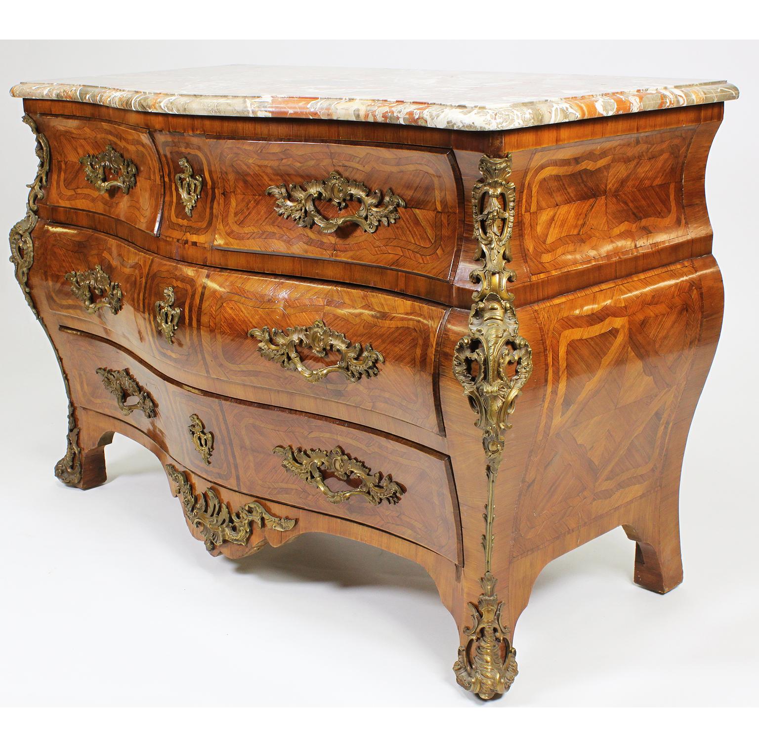 A French Regency Revival 19th/20th Century Transitional Louis XV/XVI Style Gilt-Bronze Mounted Kingwood and Tulipwood Parquetry Five-Drawer Commode with Marble Top. The bombé serpentine form body with a veined marble top above two upper drawers and