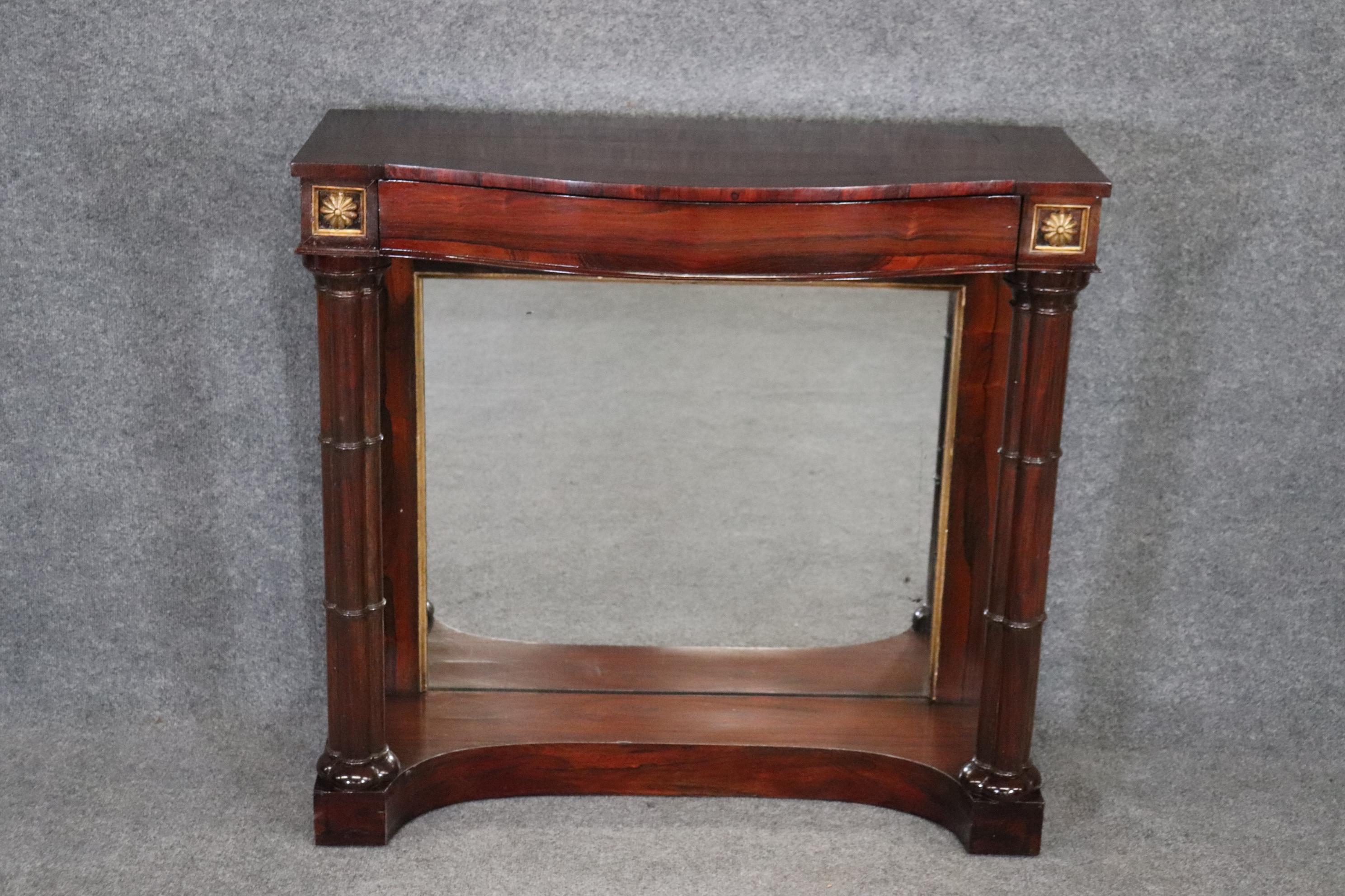 This is gorgeous French Empire rosewood and rosewood banded console table in the French regency style dating to the 1860s era with a mirrored back and giltwood florets. The table is in good original condition with gold leaf gilded details and