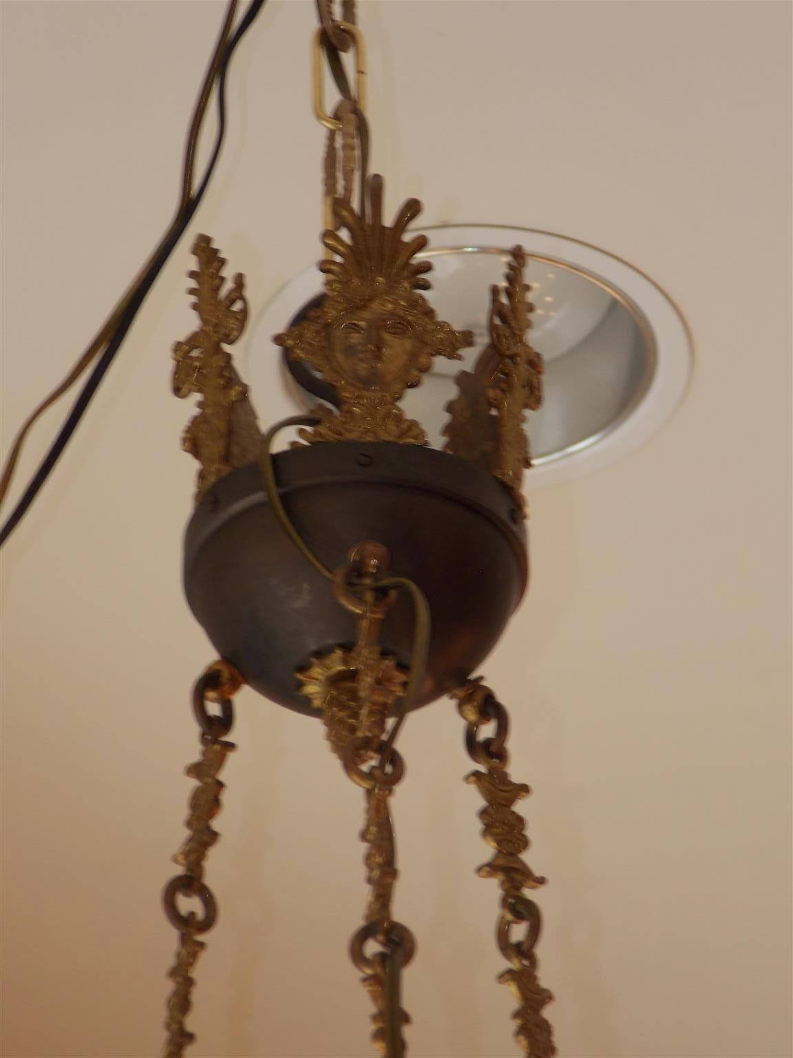 French Regency gilt bronze and painted hanging chandelier with a centered mask and palmette canopy, cascading floral chain, six scrolled palmette medallion griffon arms, Pegasus adornments, and terminating with a centered flame finial with flanking