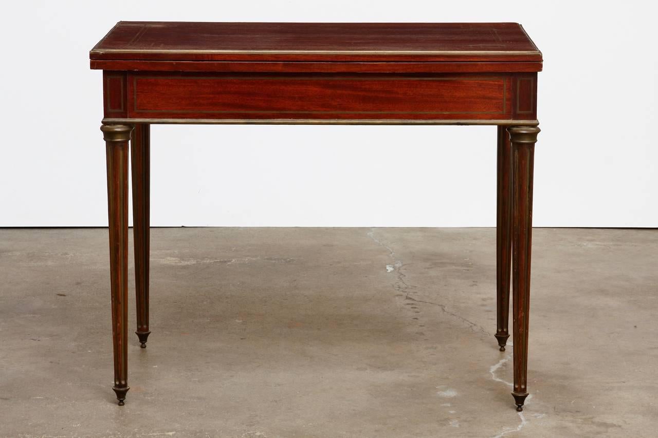 Elegant 19th century French regency flip-top game table made in the neoclassical taste. Features a mahogany case decorated with a fine brass inlay and brass mounts on the edges and legs. The table opens to a large decorated game board with a French